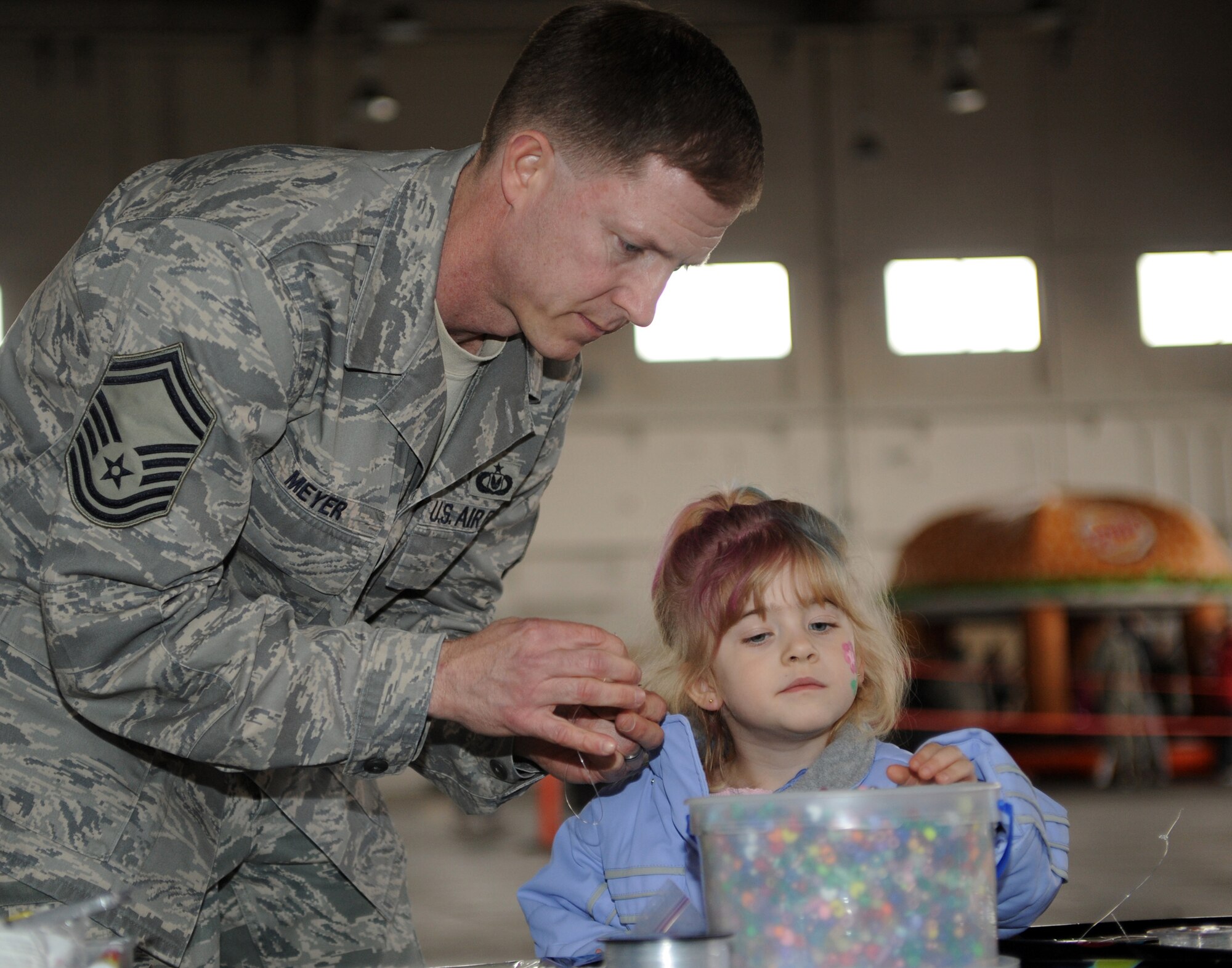 Senior Master Sergeant Charles Meyer and his daughter, Julia, build a beaded necklace at the Spring Break-up Party on April 24. Thanks to volunteers base-wide the Break-up party is a success of family fun for all military members each year. The Break-up party is the time of the year when military members and their families can get together and have family fun for hours on end.(U.S. Air Force photo by Senior Airman Laura Turner)