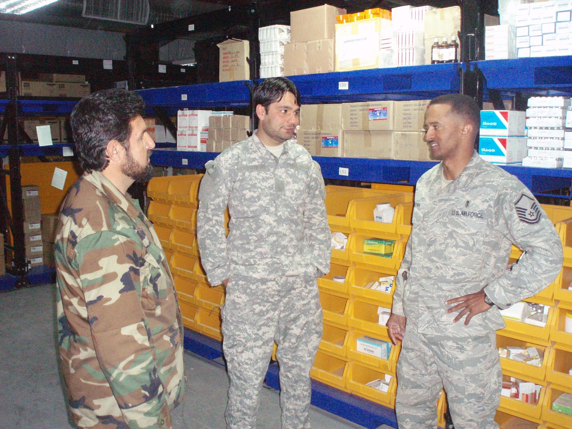 Master Sgt. Dewane Brown, Medical Embedded Training Team mentor, discusses medical logistics operations with Sgt Zia, Afghan National Army regional hospital warehouse worker, with Sergeant Brown’s interpreter, Mr. Doust Mohammad. Sergeant Brown is helping modernize the Afghan healthcare system by bringing modern medicine, technology, and supply operations to Afghanistan. A previous healthcare system was virtually non-existent under the Taliban regime. (Courtesy photo)