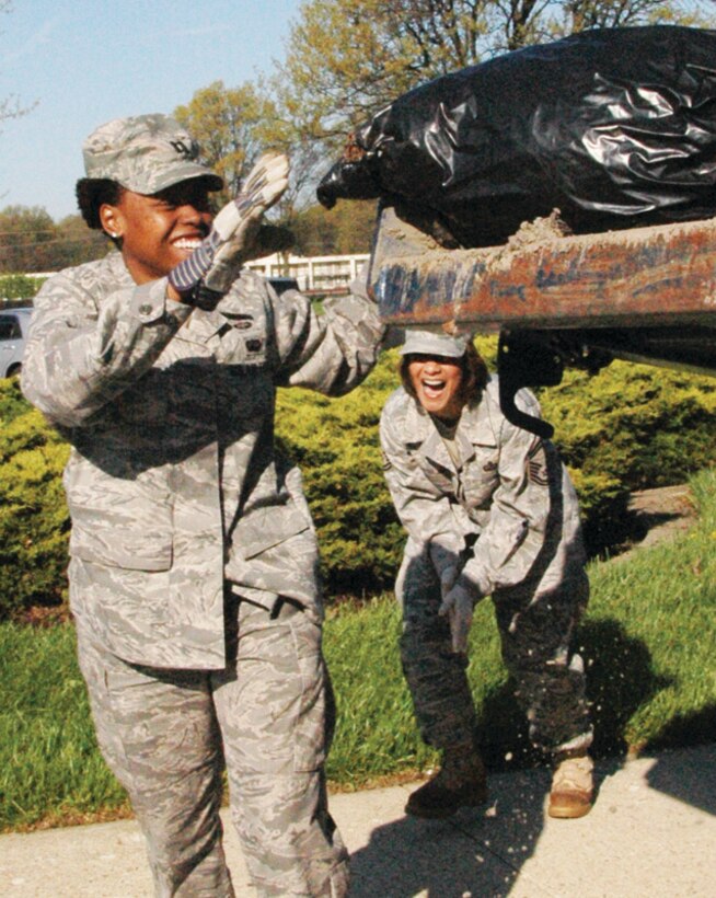 Captain Shayla Canty, 316th Contracting Squadron team lead base support contracting officer, and Senior Master Sgt. Miriam Riegler, 316 CS superintendent, have fun bagging and tossing trash bags of debris on to a flatbed truck during the facility focus clean up portion of Earth Day activities April 24. (U.S. Air Force photo/ Bobby Jones)