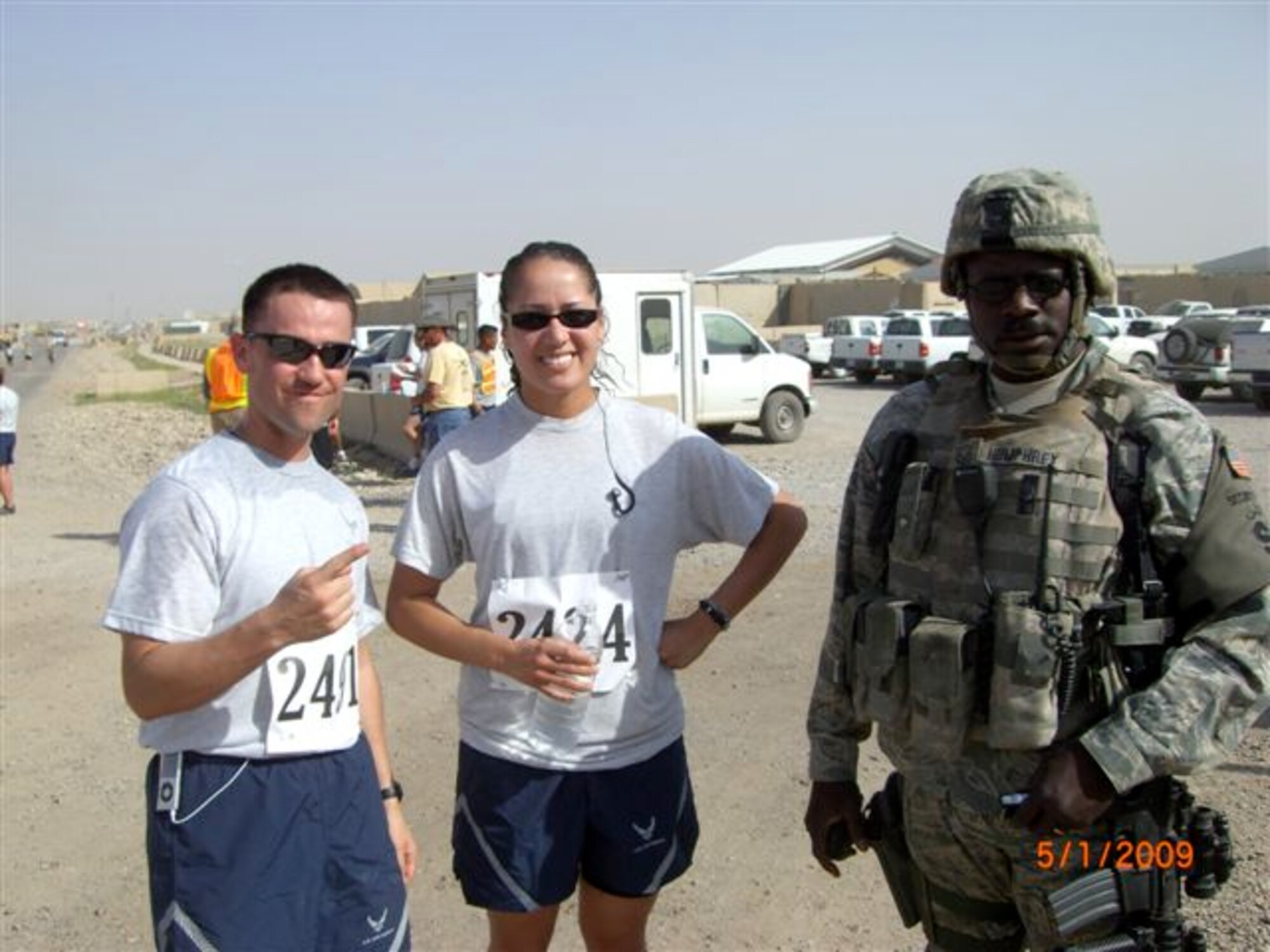 Tech. Sgt. Sam A. Ruiz and Senior Airman Sheryl N. Job, both from the 119th Wing Security Forces Squadron, North Dakota Air National Guard take a break after running in a 5K race in Iraq.  Master Sgt. Albert C. Humphrey, also from the 119th Wing Security Forces Squadron, came to the race directly from his work shift still dressed in his gear to show support for his fellow Happy Hooligans participating in the race.