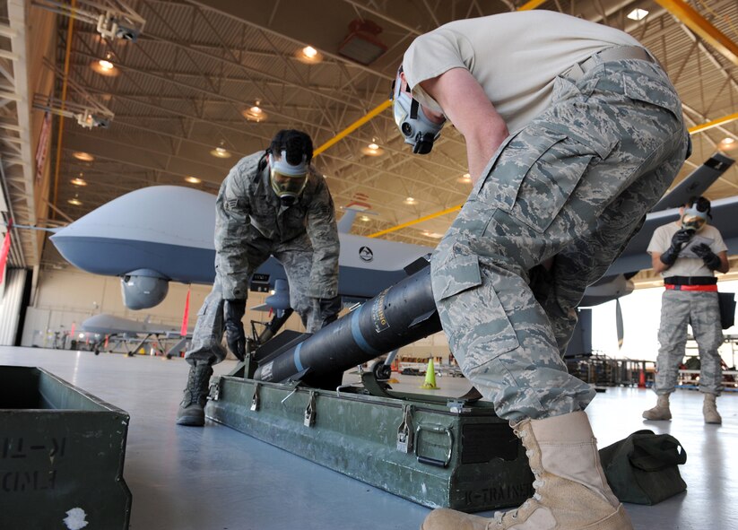 CREECH AFB, Nev. -- Senior Airmen Gale Passe (left) and Jason Atwell, both MQ-9 Reaper weapon loaders assigned to the 432d Aircraft Maintenance Squadron, prepare to load an AGM-114 Hellfire II air-to-ground missile onto the MQ-9 during weapons load training at Creech April 22. Load crew members were also required to wear their gas mask to simulate loading in a hostile environment. (U.S. Air Force photo/Senior Airman Larry E. Reid Jr.)