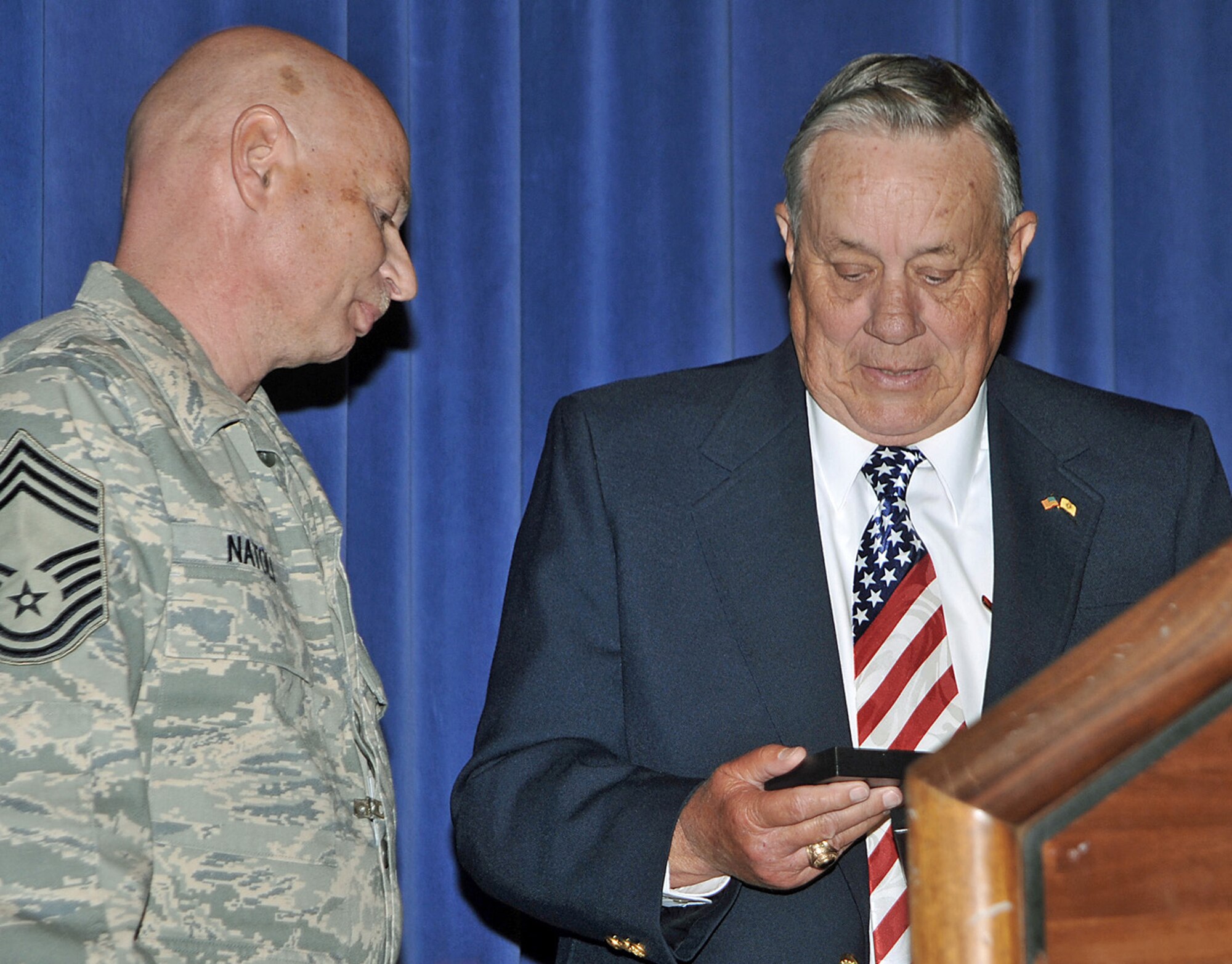 Retired Maj. Kenneth Carpenter receives a decorative coaster from Chief Master Sgt. David Natoli following his Year of Leadership speech at the Peterson Air Force Base auditorium April 27. The blue and silver coasters, which are made of glass and metal, are given to visiting distinguished visitors as a token of appreciation for their support of Peterson AFB Airmen and the United Stated Air Force. Chief Natoli is the 721st Mission Support Group superintendent. (U.S. Air Force photo/Dennis Howk)