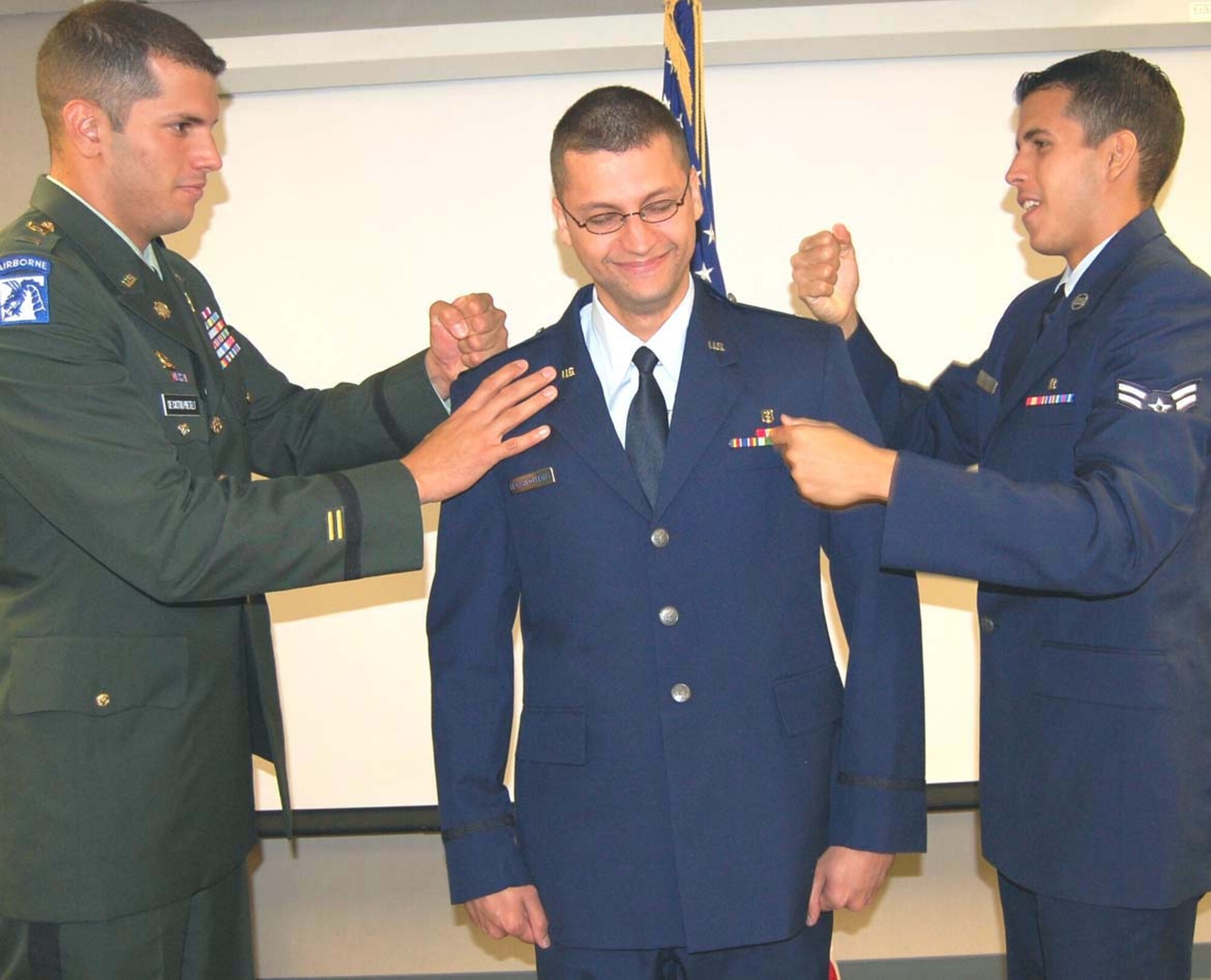 Lieutenant De Castro, left, and Airman De Castro, right, simulate “pounding” new captain’s bars on Captain De Castro during the promotion ceremony.  (U.S. Air Force photo by Steve Pivnick)