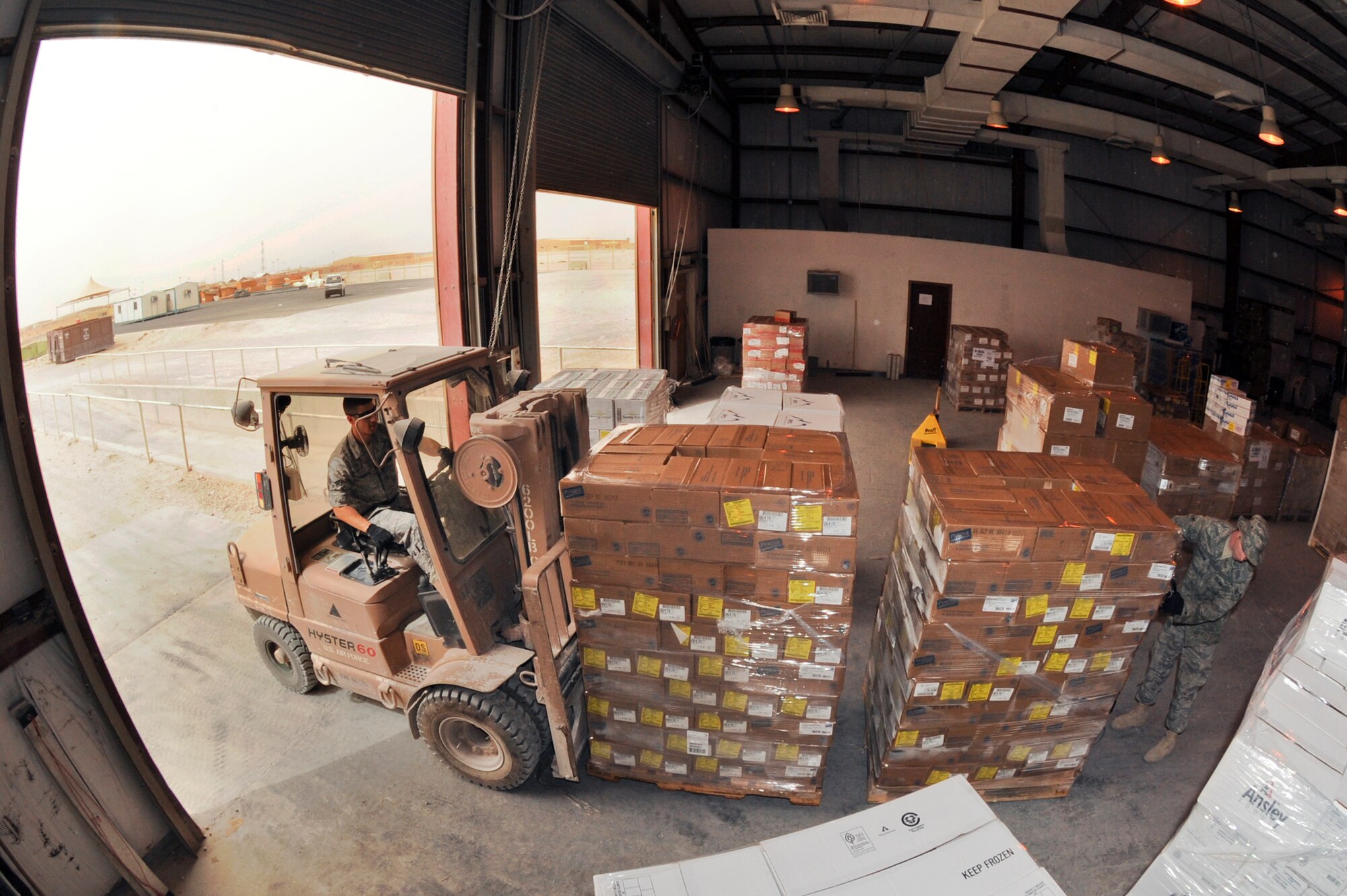 Senior Airman Leandro Corchado, a rations clerk with the 379th Expeditionary Force Support Squadron, uses a forklift to transfer a pallet of food to a cold storage container as Airman 1st Class Martin Richardson, stages the next pallet to be moved out from the cold store house here, May 6, 2009, in an undisclosed location in Southwest Asia.  The rations flight process over 81,000lbs of food weekly.  Airman Corchado hails from Miami, Fla., and is deployed from Nellis Air Force Base, Nev. and Airman Richardson is native to Conway, Ark. and is deployed from Little Rock Air Force Base, Ark., both in support of Operations Iraqi and Enduring Freedom and Combined Joint Task Force - Horn of Africa.  (U.S. Air Force Photo by Staff Sgt. Joshua Garcia/released)