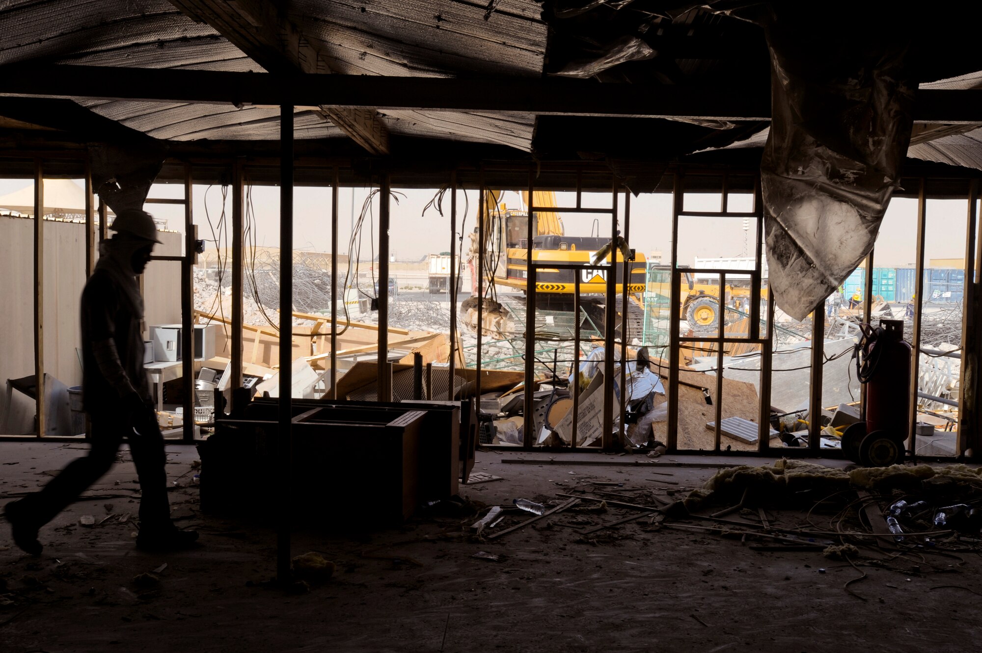 A contract worker walks inside the Old Independence Dining Facility during its demolition as heavy machinery is used to tear out the concrete in the background, May 5, 2009, in an undisclosed location in Southwest Asia.  The Independence DFAC was recently replaced by a new facility nearby with state of the art kitchen equipment to serve servicemembers on base.  The facility supports operations of the 379th Air Expeditionary Wing and Operations Iraqi and Enduring Freedom and Combined Joint Task Force - Horn of Africa.  (U.S. Air Force Photo by Staff Sgt. Joshua Garcia/released)