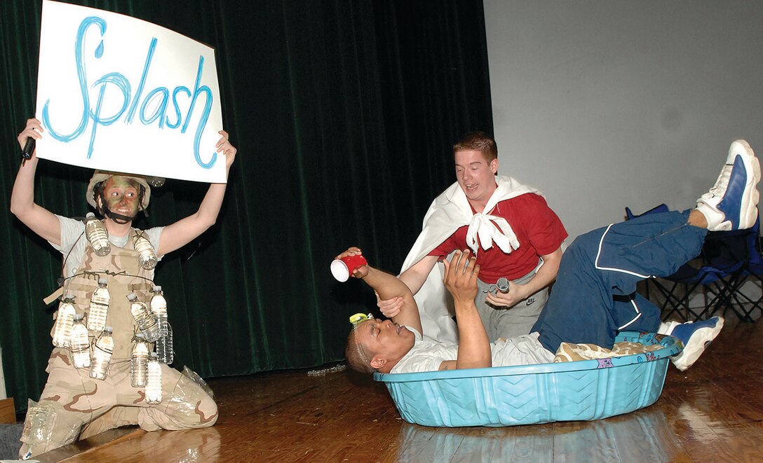 Staff Sgt. Rebekah Spedaliere, 316th Security Forces Squadron commander’s executive, holds a cue card for the audience as Airman 1st Class Louis Settle, 316th Comptroller Squadron finance technician (portraying Super Wingman) saves his friend, Staff Sgt. Charles Wilson, 316th Force Support Squadron assistant NCO in charge of career development, from drowning while under the influence of alcohol during a pool party that was part of a skit performed at the base theater May 1. The skit, during the 316th Wing commander’s call, highlighted the importance of safety during the 101 Critical Days of Summer. The skit also illustrated how Airmen should be aware of the consequences of drinking and driving, as well as drinking during outdoor activities. (U.S. Air Force photo/ Senior Airman Giang Nguyen)