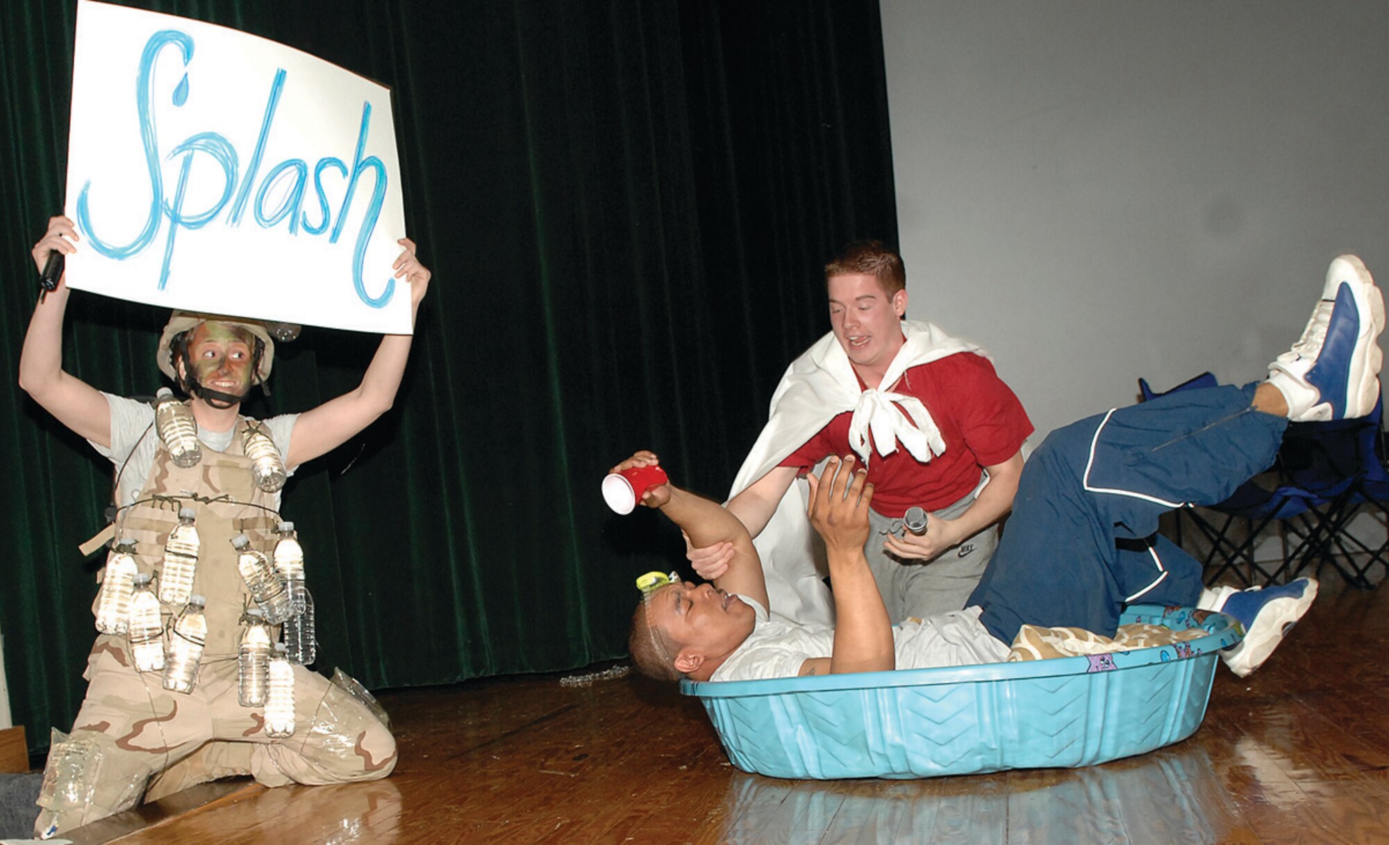 Staff Sgt. Rebekah Spedaliere, 316th Security Forces Squadron commander’s executive, holds a cue card for the audience as Airman 1st Class Louis Settle, 316th Comptroller Squadron finance technician (portraying Super Wingman) saves his friend, Staff Sgt. Charles Wilson, 316th Force Support Squadron assistant NCO in charge of career development, from drowning while under the influence of alcohol during a pool party that was part of a skit performed at the base theater May 1. The skit, during the 316th Wing commander’s call, highlighted the importance of safety during the 101 Critical Days of Summer. The skit also illustrated how Airmen should be aware of the consequences of drinking and driving, as well as drinking during outdoor activities. (U.S. Air Force photo/ Senior Airman Giang Nguyen)