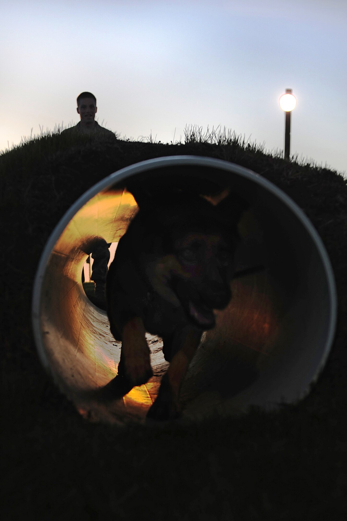 Senior Airman William Knight, 28th Security Forces Squadron dog handler, watches as Rex, a 28 SFS military working dog, runs through a tunnel in the obstacle course, here, May 7.  Military working dogs perform obedience training to ensure they listen to their handler. (U.S. Air Force photo/Airman 1st Class Joshua J. Seybert)