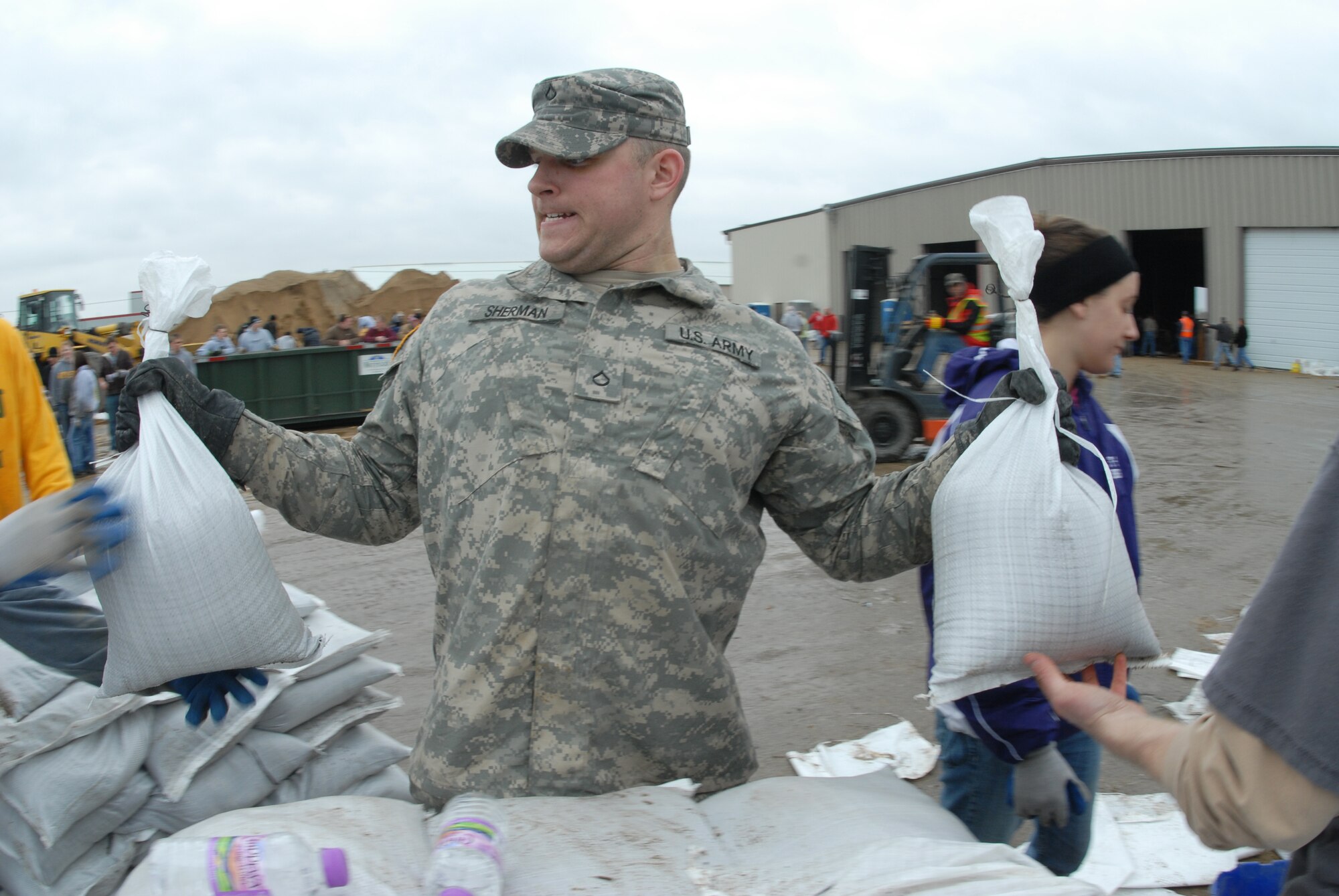 Pfc. Bradley Sherman, of the 815th Engineer Company, passes sandbags to civilian flood fighting volunteers Mar. 23, at what has become known as 'sandbag central' at the Fargo City garage.  The sandbags were loaded on trucks and delivered to various flood fighting locations along the Red River.  Sherman is from the Lisbon-Lamoure, N.D. area.