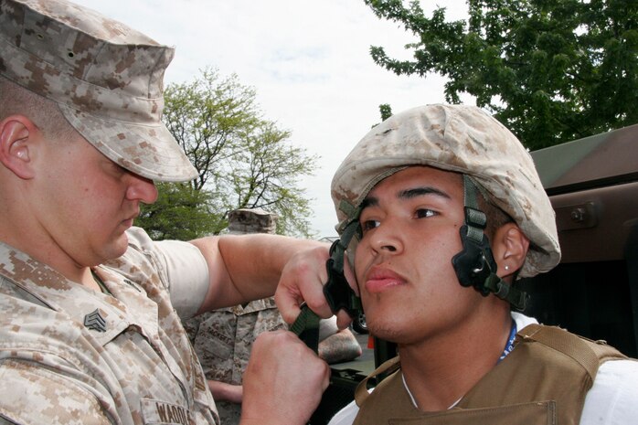 Sgt. Jared B. Waddle secures the chinstrap of a Kevlar helmet on Esteban Valtierra, a 16-year-old Marie Curie High School junior during a static display at Marie Curie High School May 11 as part of the inaugural Marine Week Chicago. The static display at Chicago's second largest high school was one of the first events of the inaugural Marine Week Chicago. Marine Week Chicago, which runs from May 11-17, is an opportunity for Chicago citizens to meet the men and women of the Marine Corps and learn about its history, traditions and value to the nation.