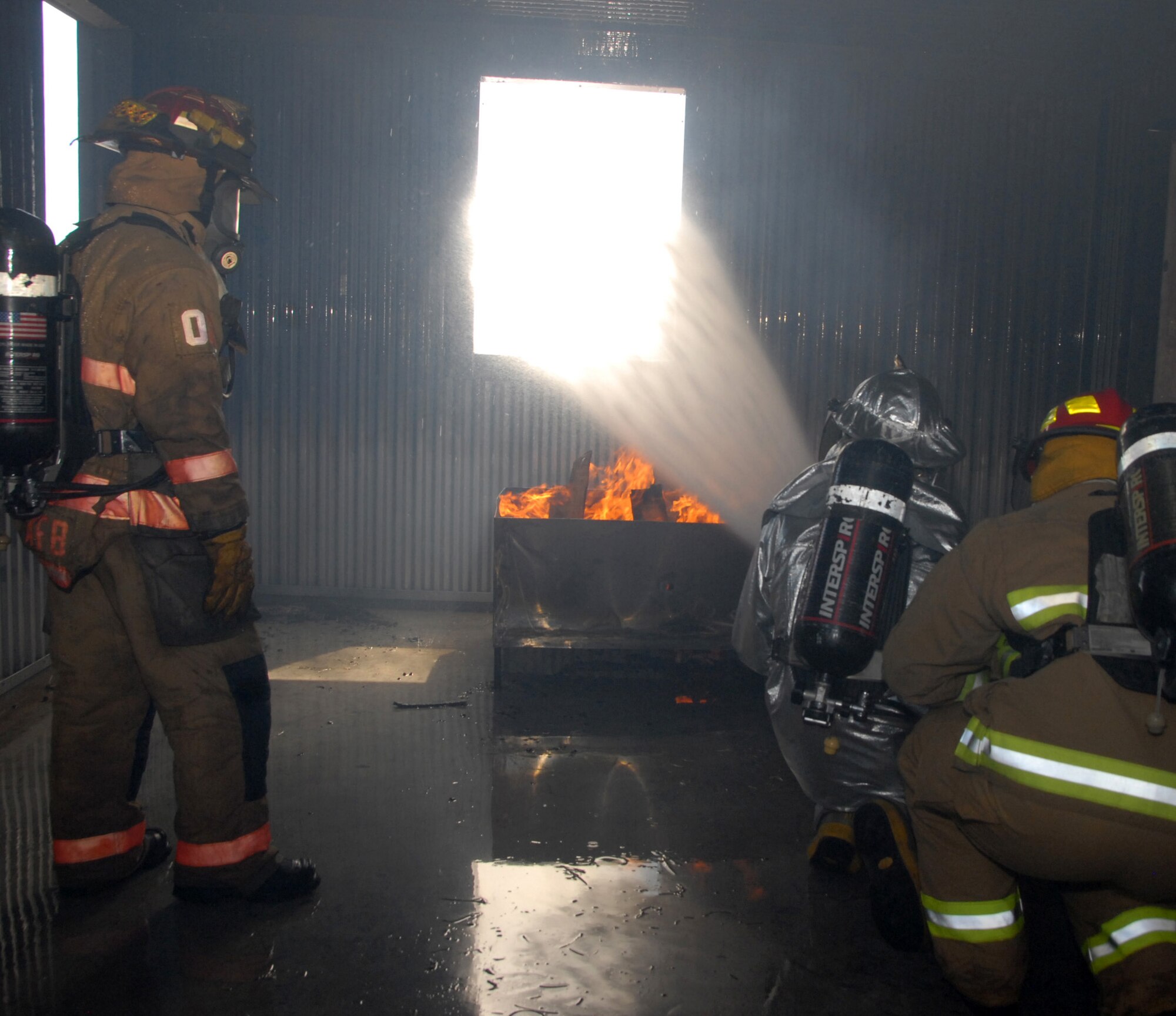 Altus Air Force Base, Okla. -- Firefighters from the Altus Air Force Base Fire department perform a ventilation tactic called fog streaming during a training exercise held on base on April 4. This tactic entails hydraulically ventilating heated smoke and gasses from the room in order to rapidly provide the room with fresh air. The fire department uses a fire structural trainer for live burns. The quarterly-held training is conducted by military and civilian firefighters. (U.S. Air Force by photo/Senior Airman Cherice Bryant)