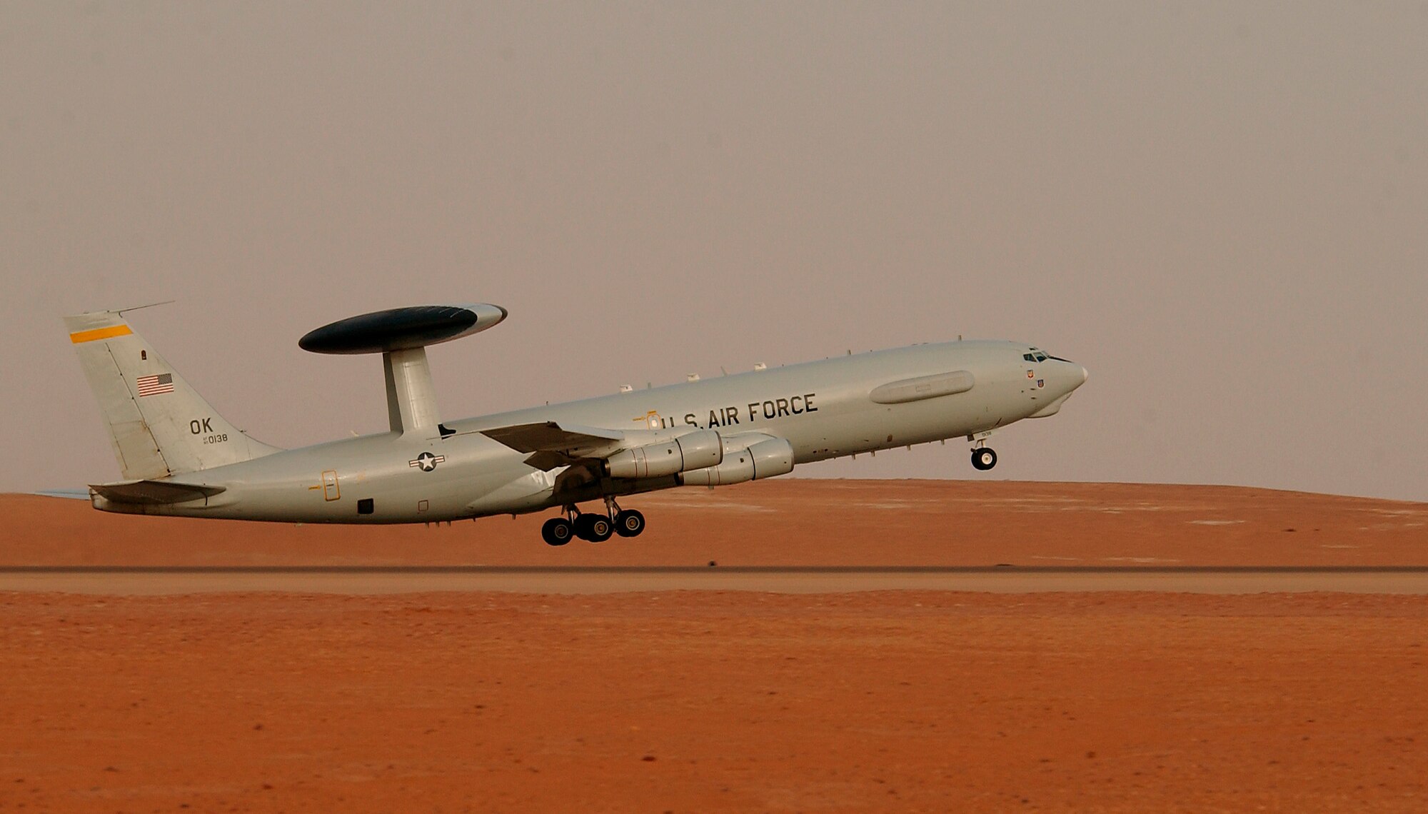 An E-3 Senty AWACS takes off in the desert.