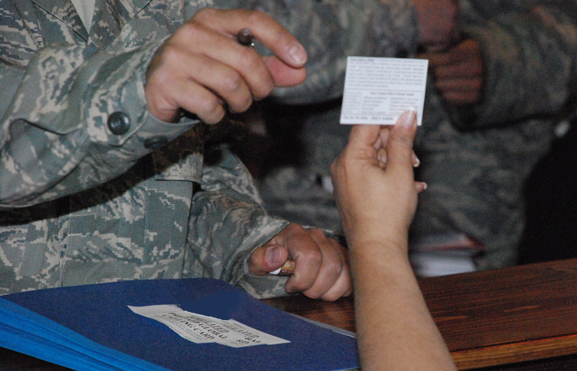 Kathy McCoole, 90th Missile Wing sexual assault response coordinator, hands an information card to a member of the inprocessing line during the exercise May 1.