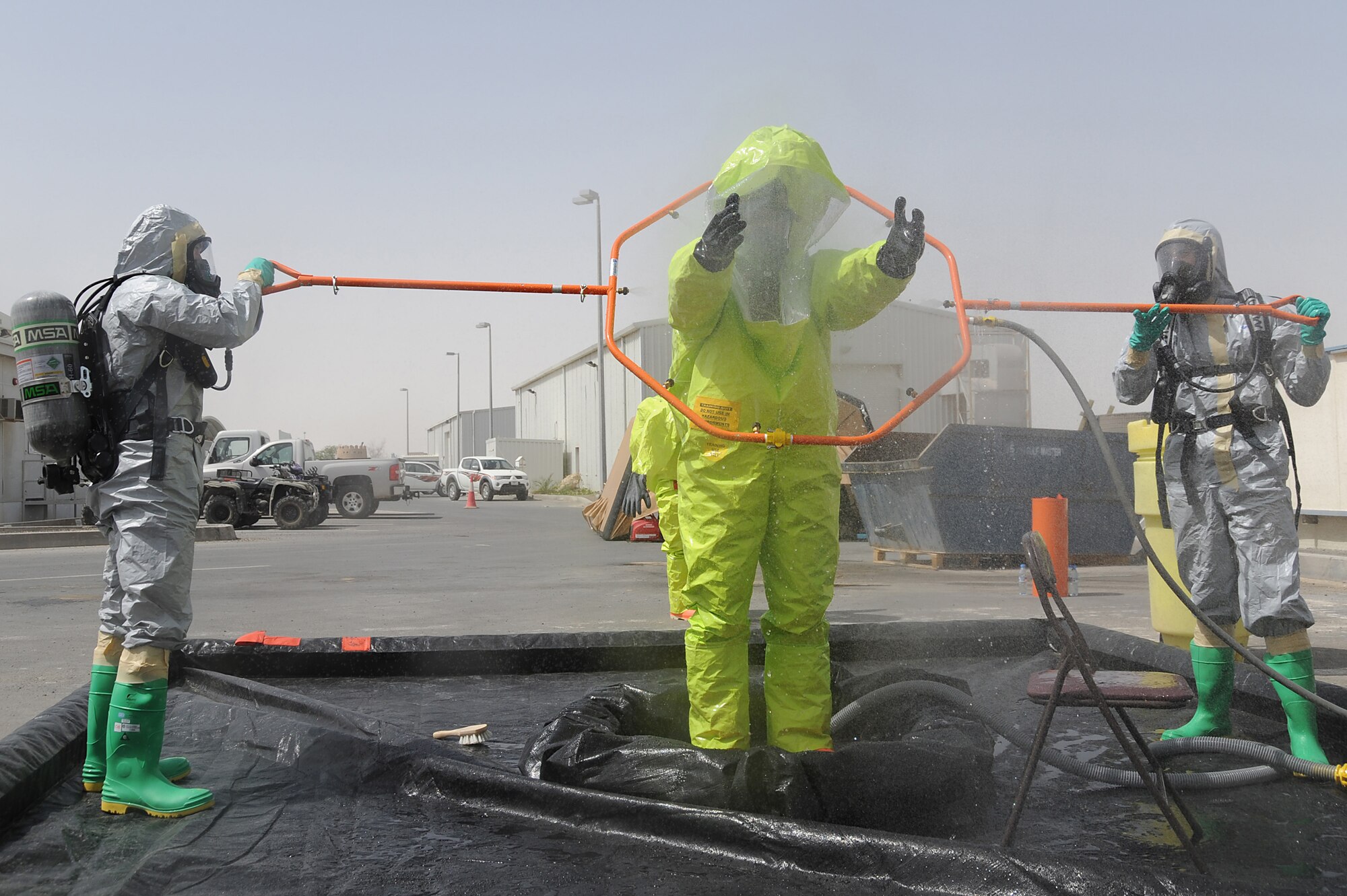 Senior Airman Bradley Cook processes through a decontamination area while Master Sgt. Jason Golden and Staff Sgt. Bobo wash off his level-A hazmat suit of contaminants during hazmat decontamination training, May 2 at an undisclosed location in Southwest Asia. All three Airmen are with the 380th Expeditionary Civil Engineer Squadron Readiness and Emergency Management Flight. The flight performs Chemical, Biological, Radiological, and Nuclear (CBRN) detection and decontamination operations as well as emergency management command and control. (U.S. Air Force photo by Senior Airman Brian J. Ellis) (Released)