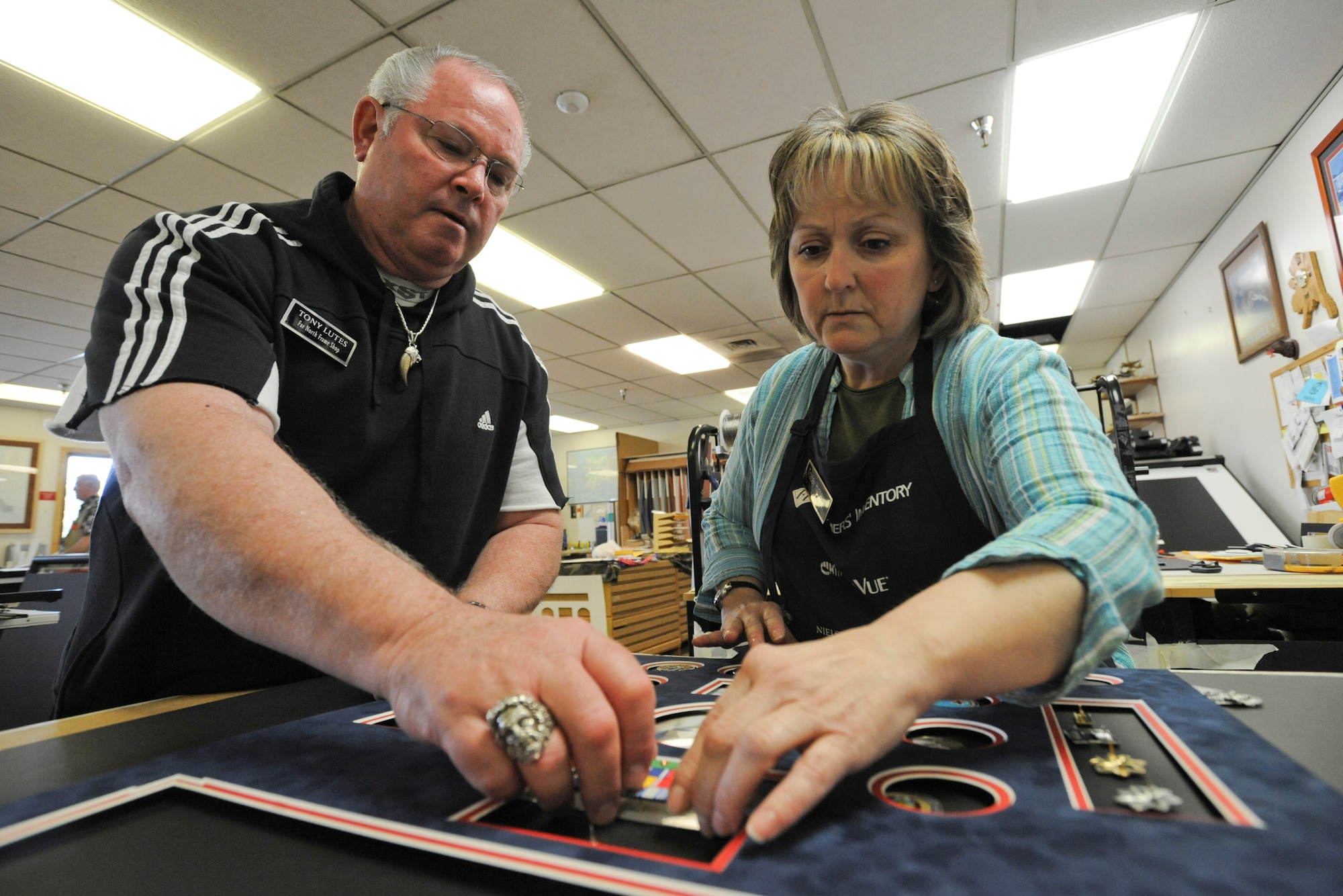 ELMENDORF AIR FORCE BASE, Alaska -- Tony Lutes and Tracey Hunnwell, 3rd Services Squadron coordinators, place accouterments in the matting for a retirement shadow box at the Arts and Craft Center, May 5, 2009. The center provides services to military members and their families varying from shadow boxes, plaques, pottery, glass blowing and many more styles of art.(U.S. Air Force photo/Senior Airman Matthew Owens)