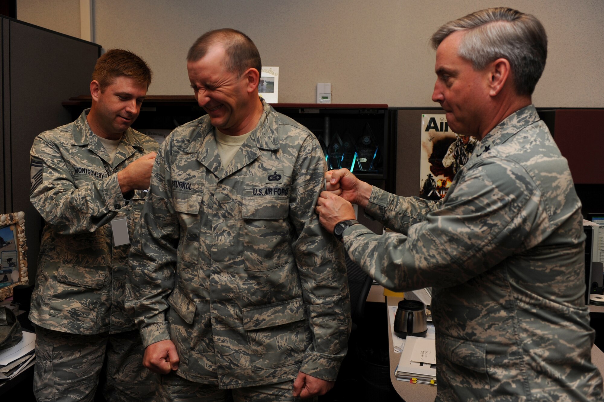 Major Gen. Kip Self, U.S. Air Force Expeditionary Center commander, and Senior Master Sgt. Michael Montgomery, Expeditionary Center Public Affairs superintendant, tack master sergeant stripes on Tech Sgt. Scott Sturkol, Expeditionary Center Public Affairs NCO in charge, on May 14 at the center.  Ten Airmen from the Expeditionary Center were selected for E-7 stripes. (U.S. Air Force Photo/Staff Sgt. Nathan G. Bevier) 