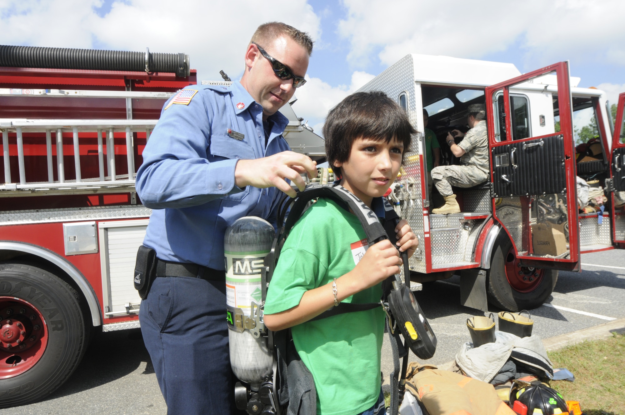 Robins firefighter Daniel Connelly helps Jonathan Morreira try on a self contained breathing apparatus that firefighters wear at the  REACH picnic at Robins Park April 30. U. S. Air Force photo by Sue Sapp