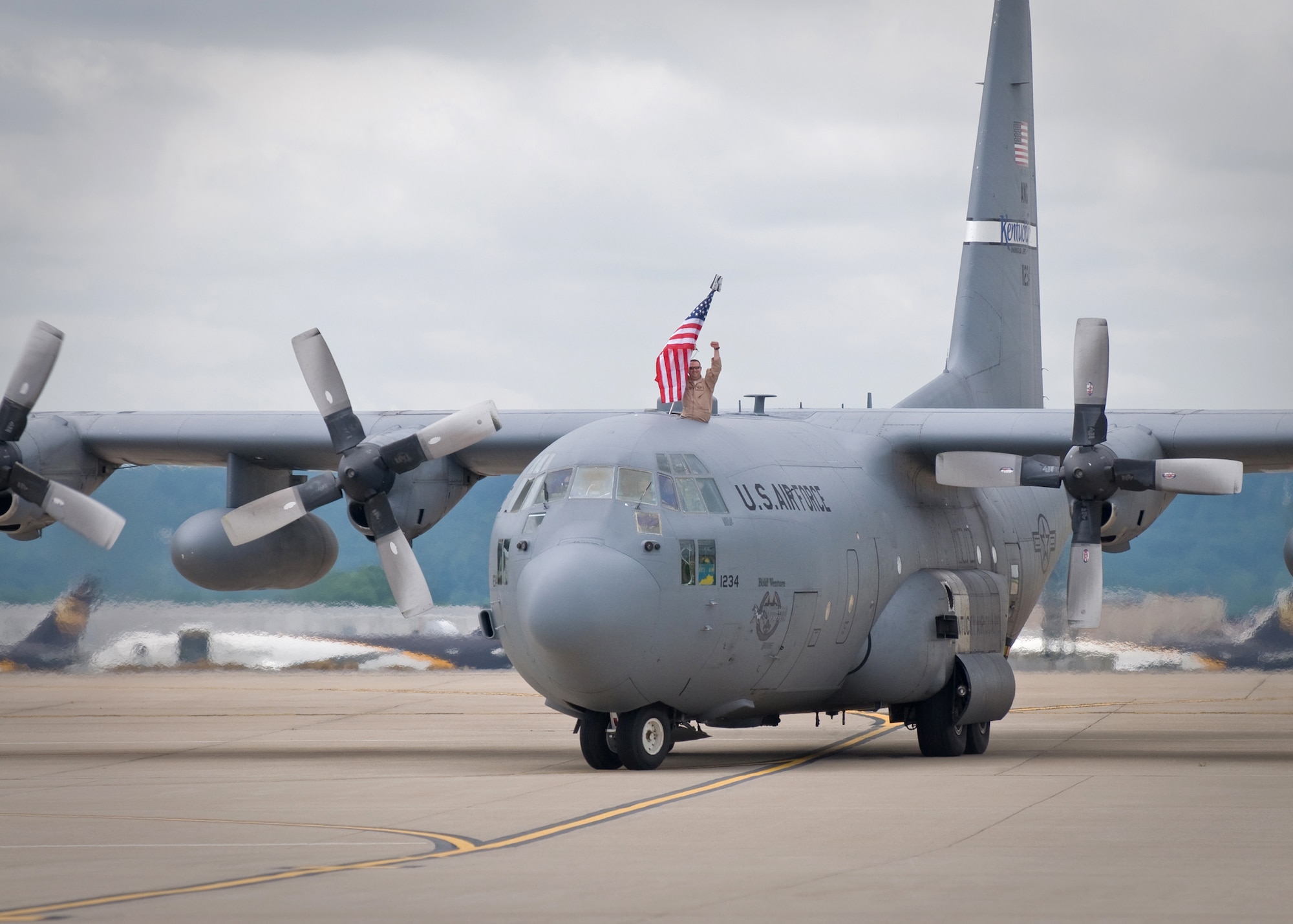 A Kentucky Air Guardsman displays the colors as a C-130 from the 123rd Airlift Wing taxis to a stop on the flightline of the Kentucky Air National Guard Base in Louisville, Ky., on May 16, 2009. The aircraft and its passengers were returning from a two-month deployment to Afghanistan for Operation Enduring Freedom. (USAF photo by Capt. Dale Greer.)