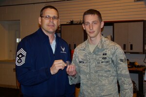 Senior Airman Adam Smith, 1st Civil Engineering Squadron emergency management journeyman, receives a coin from Command Chief Master Sergeant Kevin Slater during a suprise ceremony here April 13.  Airman Smith was recognized for performing CPR and saving a man's life at a local supermarket April 7.