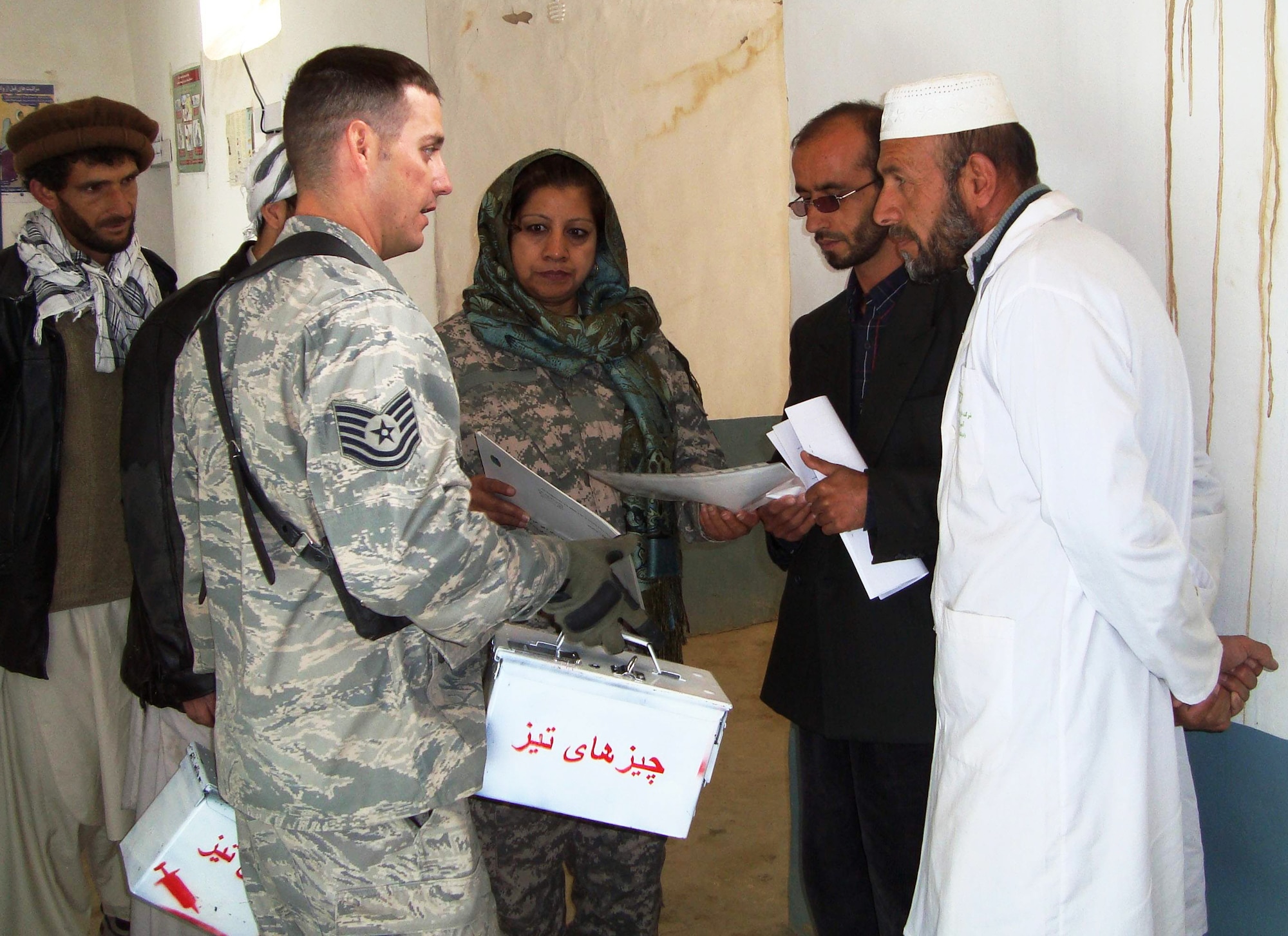 Tech. Sgt. James Bailey provides Pharmacist Mohammad Yagub (right) and Ghulam Maiudin, a vaccinator, with containers to properly dispose of needles and other biohazardous materials during a visit to the Peshgor Clinic in Khenj District, Afghanistan. Sergeant Bailey is a Panjshir  Provincial Reconstruction Team medic. (U.S. Air Force photo/Maj. Valerie Trump) 
