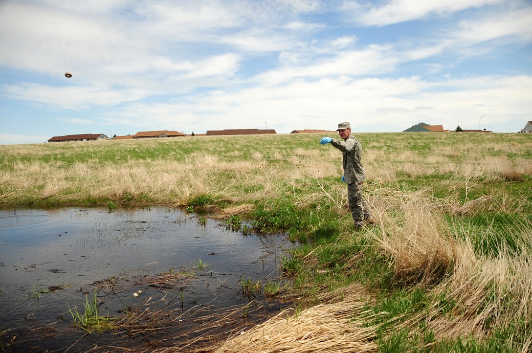 Airman 1st Class Corey Turpin, 28th Civil Engineer Squadron pest management apprentice, tosses larvicide into a pool of water, May 14.  The larvicide keeps mosquitoes in their larvae stage to stop them from maturing. (U.S. Air Force photo/Senior Airman Anthony Sanchelli)