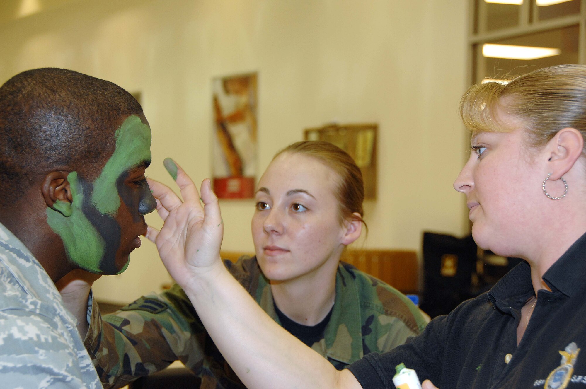 OFFUTT AIR FORCE BASE, Neb. - Senior Airman Timothy Terrell, 55th Security Forces Squadron, has his face painted with camoflauge paint by Airman 1st Class Tara Hensley, 55th SFS, center, and Sharon Labenburg, 55th SFS, during a military weapon display at the Base Exchange here May 15. The display was a part of National Law Enforcement Week. U.S. Air Force Photo by Dana P. Heard