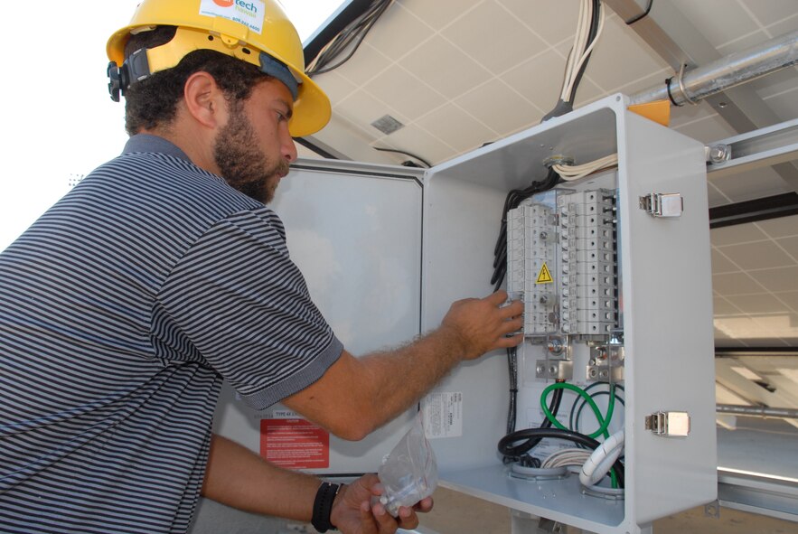 HICKAM AIR FORCE BASE, Hawaii – Nolie Diakoulas, Sunetric project engineer, installs fuses in the combiner box behind the solar panels here May 13. When the sun hits the photo voltaic panels, electrons move from front to back, creating a current that travels through small wires to a junction box in the back. The junction box takes the current from the small wires and moves it to larger wires, which travel to a combiner box. There, DC power is converted to AC (usable) power, which runs the base hydrogen station. The combination of solar panels with the hydrogen station here makes the project a dynamic, first-in-the-Air Force and first-in-Hawaii combination. (U.S. Air Force photo by Senior Airman Carolyn Viss)