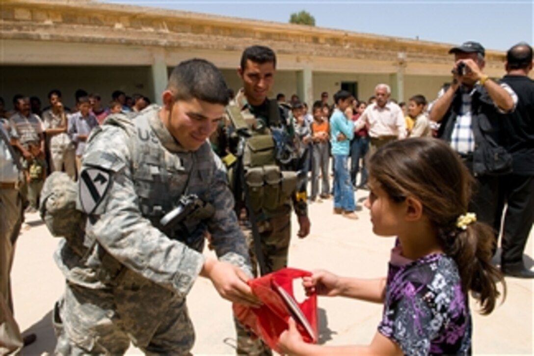 U.S. Army 1st Lt. Jacob Lopez, a platoon leader from Crazy horse Troop, 4th Squadron, 9th Cavalry Regiment, 2nd Brigade Combat Team, 1st Cavalry Division, Fort Hood, Texas, gives a bag with school supplies to an Iraqi girl in the village of Tubazawa, in Kirkuk, Iraq, on May 14, 2009.  
