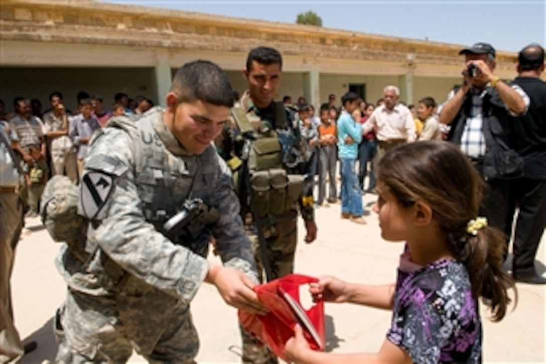 U.S. Army 1st Lt. Jacob Lopez, a platoon leader from Crazy horse Troop, 4th Squadron, 9th Cavalry Regiment, 2nd Brigade Combat Team, 1st Cavalry Division, Fort Hood, Texas, gives a bag with school supplies to an Iraqi girl in the village of Tubazawa, in Kirkuk, Iraq, on May 14, 2009.  