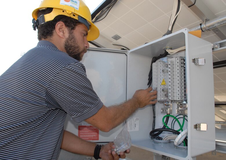 Nolie Diakoulas installs fuses in the combiner box behind the solar panels May 13 at Hickam Air Force Base, Hawaii. When the sun hits the photovoltaic panels, electrons move from front to back, creating a current that travels through small wires to a junction box in the back. The junction box takes the current from the small wires and moves it to larger wires, which travel to a combiner box. There, DC power is converted to AC (usable) power, which runs the base hydrogen station. Mr. Diakoulas  is a civilian contractor on the project. (U.S. Air Force photo/Senior Airman Carolyn Viss)