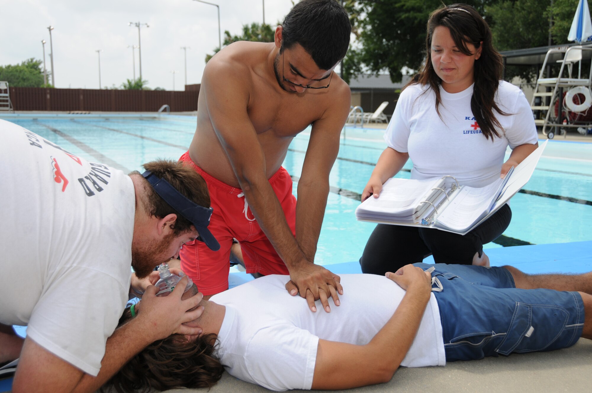 Base lifeguards Eric Lambes, left, Miguel Rivera-Ainhea and Sera Chereskin review cardiopulmonary resuscitation techniques on “victim” Logan DeLuke May 13.  The Triangle and main base pools open Saturday.    The main pool is open daily except Mondays from noon to 5:30 p.m. with lap swimming available.  A new parking lot off Meadows Drive replaces the old parking area where the new post office is being built.  The Triangle pool is open daily except Wednesdays from noon to 7 p.m., with adult lap swimming 11 a.m. to noon and for all patrons during normal hours.  The cost is $1.50 daily.  Season passes are sold at outdoor recreation and both pools. An individual season pass is $20, wotj a $60 charge for a pass for three or more family members.  Ages 5 and younger swim free.  For more information, log on to http://www. keeslerservices.us and click on the link for pools.  (U.S. Air Force photo by Kemberly Groue)