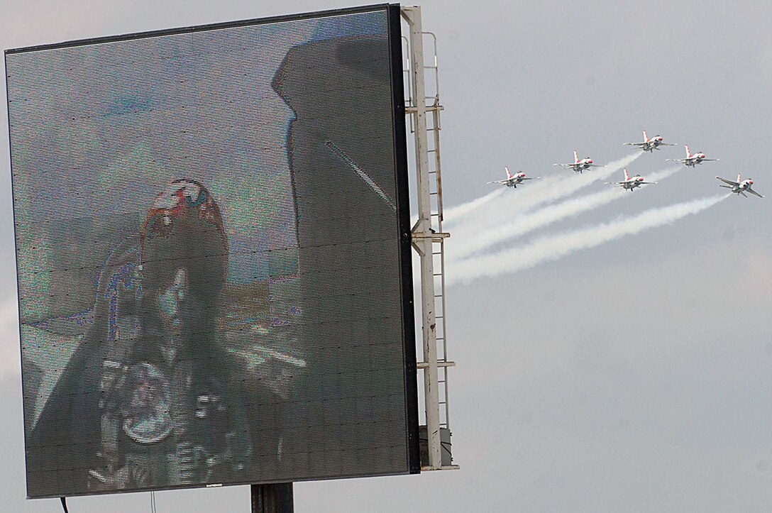 The Thunderbirds fly in formation as the Jumbo-Tron displays Lt. Col. Greg Thomas, Thunderbirds commander, during the JSOH May 16. (U.S. Air Force photo/ Senior Airman Giang Nguyen)