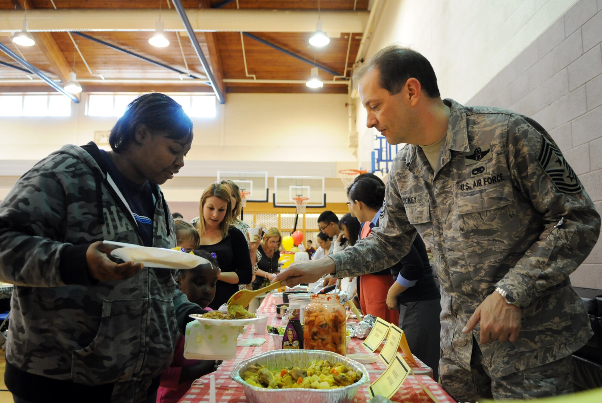 Chief Master Sgt. Antonio Hickey, 100th Air Refueling Wing command chief, serves a plate of Japanese Karagee to Felicia Smith, whose husband Darick is deployed, at the May 20 Hearts Apart event.  In addition to food, the Asian Pacific-themed event featured dance and martial arts demonstrations for American and British families of deployed servicemembers.  (U.S. Air Force photo by Staff Sgt. Austin M. May)