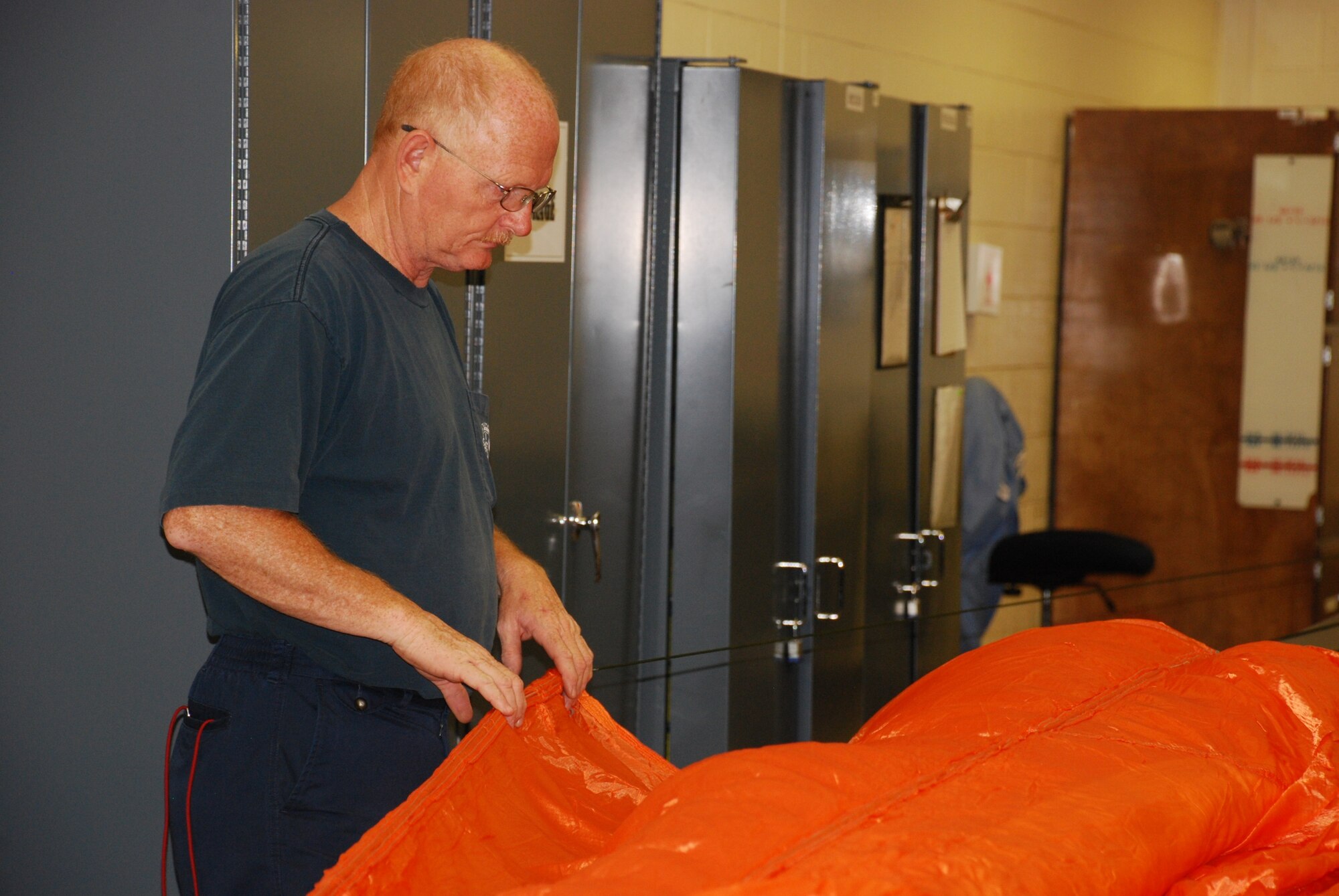 Doug Taylor, a Lier Siegler, Inc. contractor with the 80th Flying Training Wing, inspects a parachute in the fabrication shop for the Aircrew Flight Equipment shop. The orange chute is used in emergency situations when the pilot needs to be seen for a rescue mission. (U.S. Air Force photo/ Airman 1st Class Valerie Hosea)