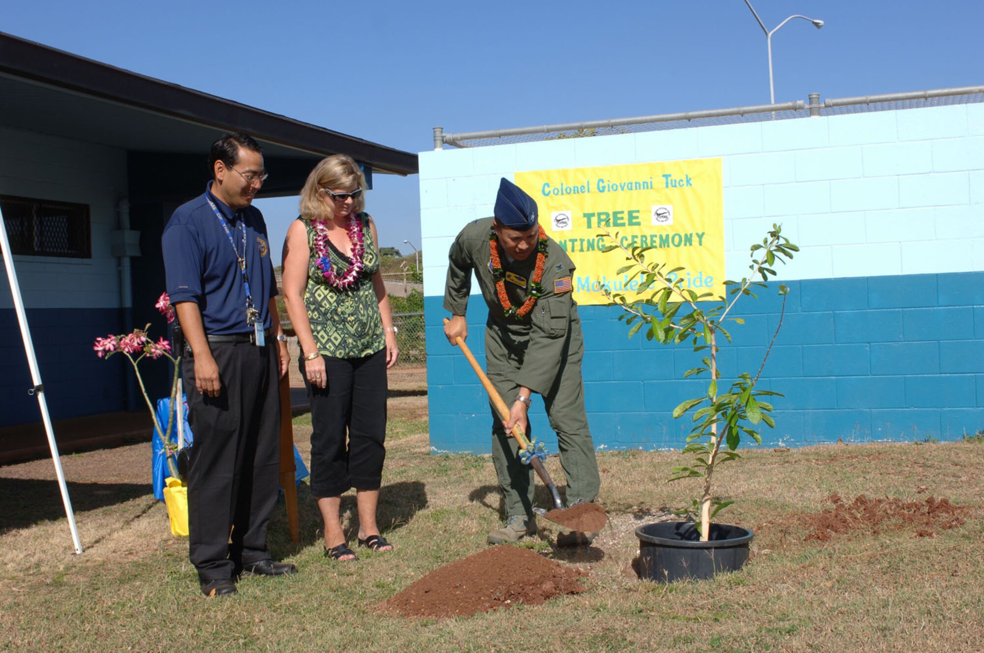 HICKAM AIR FORCE BASE, Hawaii -- Honorary guest Col. Giovanni Tuck (right), 15th Airlift Wing commander, shovels soil during a tree-planting ceremony at Mokulele Elementary School May 22 while Bart Nakamoto, the school principal (left), and Colonel Tuck's wife, Susie, (center) look on. The tree planted was an la'amia (kalabash) tree, given to him as a gift at his homecoming ceremony because he is an alumnus of the school. The tree was donated by Leroy Nagasako, a Vietnam War veteran. (U.S. Air Force photo by Oscar Hernandez)