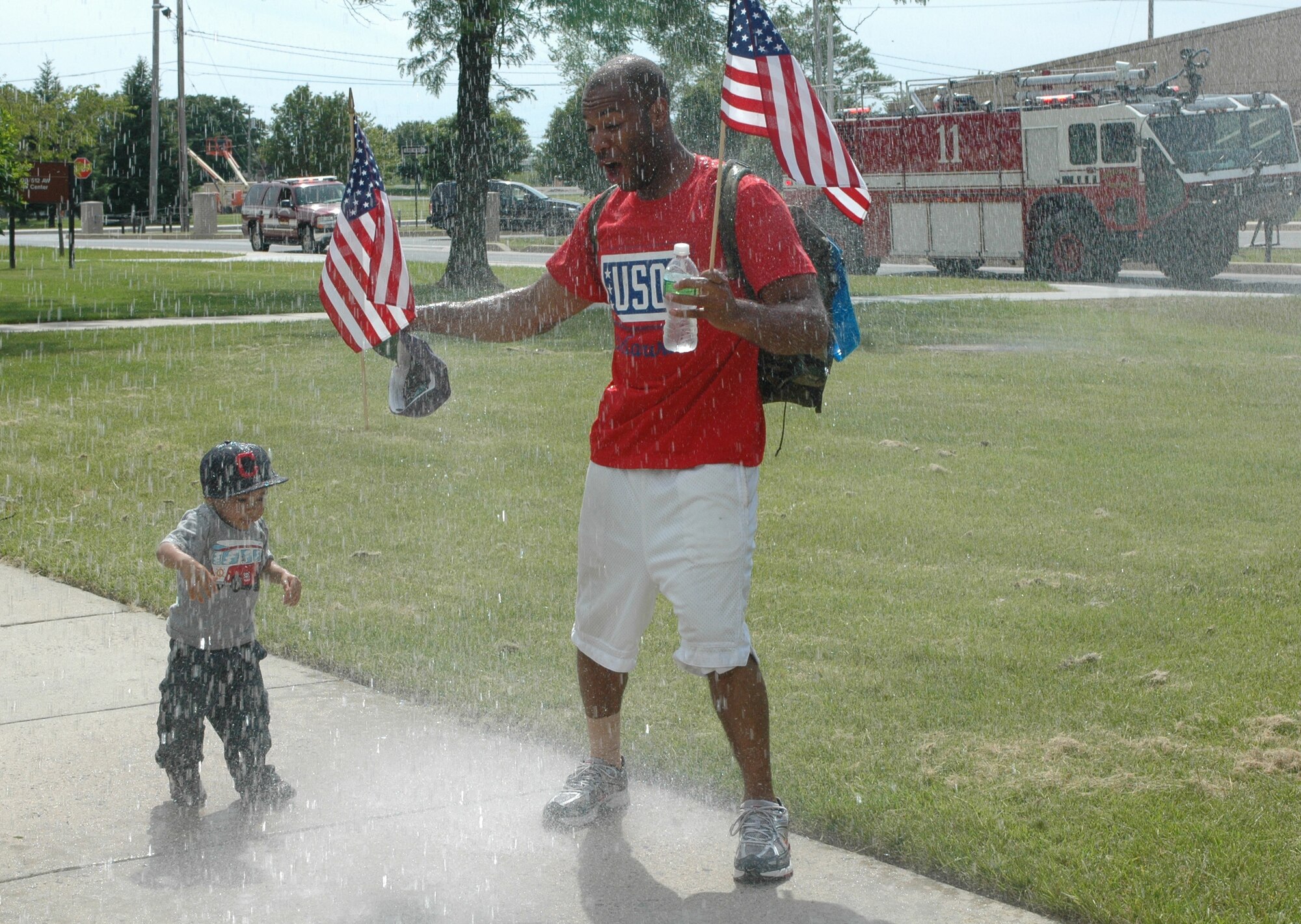 The Dover Air Force Base fire department cools off Staff Sgt. Michael Spencer and his son Devin, 2, May 22.  Sergeant Spencer, a reservist in the 512th Logistics Readiness Flight and civil servant in the 436th Logistics Readiness Squadron, completed a 47-mile ruck march from New Castle to Dover AFB May 21-22.  Eleven Airmen participated in the march part of the way and five Airmen, including Sergeant Spencer, completed the entire 47 miles to raise funds for USO Delaware. Upon their arrival they were welcomed by friends, family, wing members, and the base fire department and security forces.(U.S. Air Force photo/Capt. Marnee A.C. Losurdo)