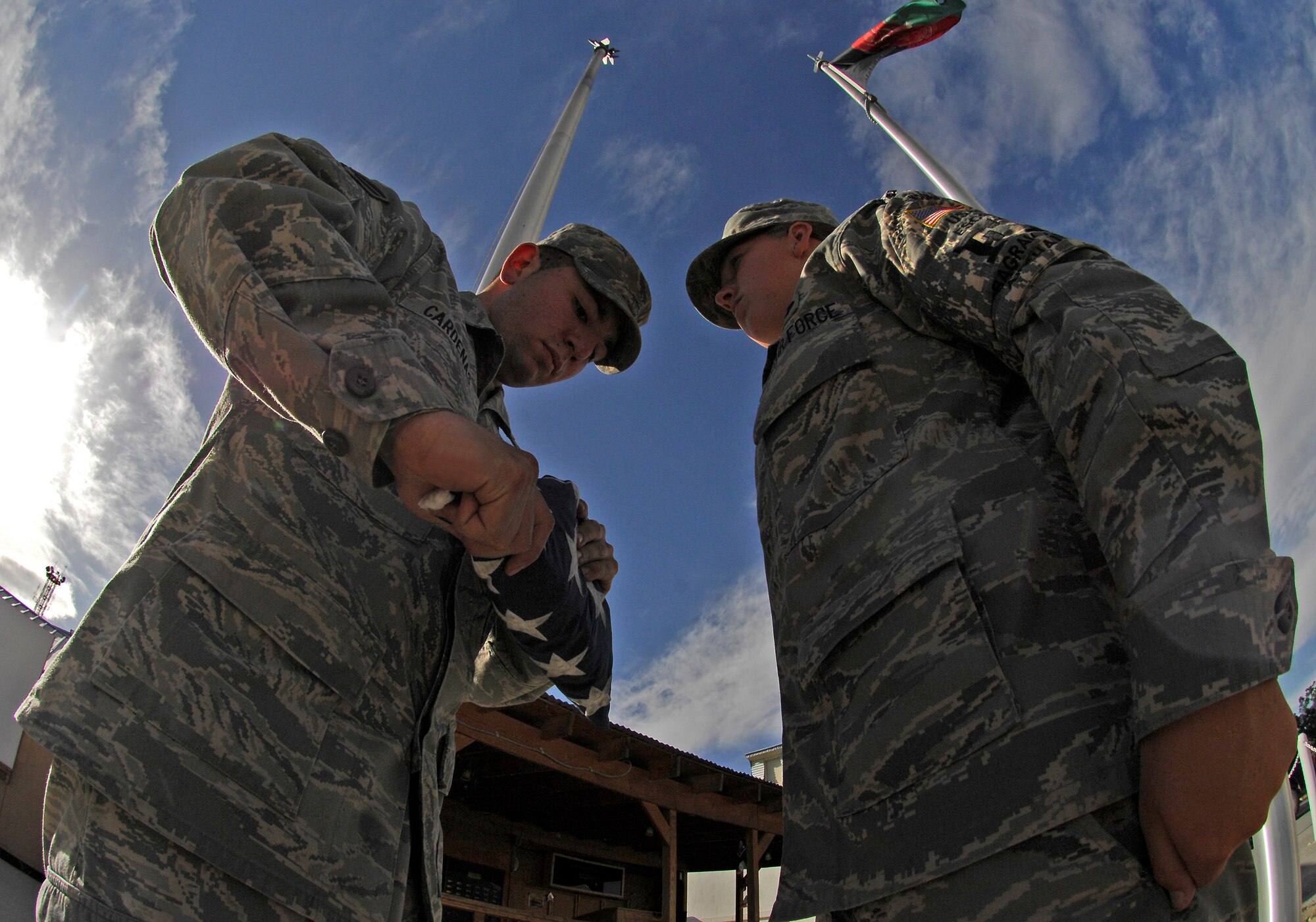 Senior Airmen Erik Cardenas, 455th Air Expeditionary Wing Public Affairs, and Christina Golden, 455th Expeditionary Civil Engineer Squadron force protection, fold the American flag during a Memorial Day ceremony at Camp Cunningham May 25. A team of seven Air Force honor guardsmen flew and folded nearly 50 flags over a three-hour period on behalf of the 455th Air Expeditionary Wing. The flags and a certificate will be sent home to friends and family of servicemembers in honor of the national holiday. (Air Force/Staff Sgt. Jason Lake) 