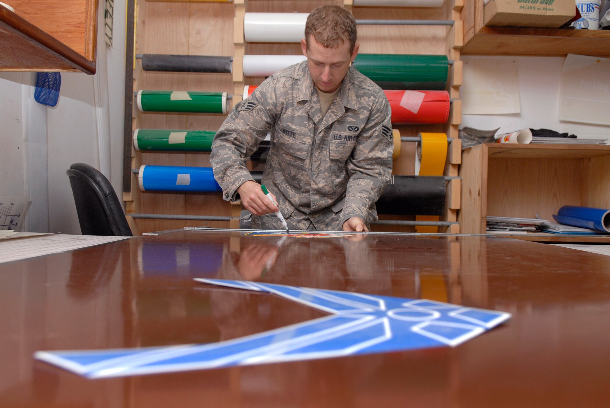 Senior Airman Geoffrey Witte, a 379th Expeditionary Civil Engineer structural journeyman, works to place vinyl emblems on a piece of sheet metal for a new Wing Operations Center sign, May 21, 2009, at an undisclosed location in Southwest Asia.  The sign shop uses an array of materials to create building, road, and other signs used throughout the base.  Airman Witte hails from Anadarko, Okla. and is deployed from Vandenberg Air Force Base, Calif. in support of Operations Iraqi and Enduring Freedom and Combined Joint Task Force - Horn of Africa.  (U.S. Air Force photo/Senior Airman Andrew Satran/released)