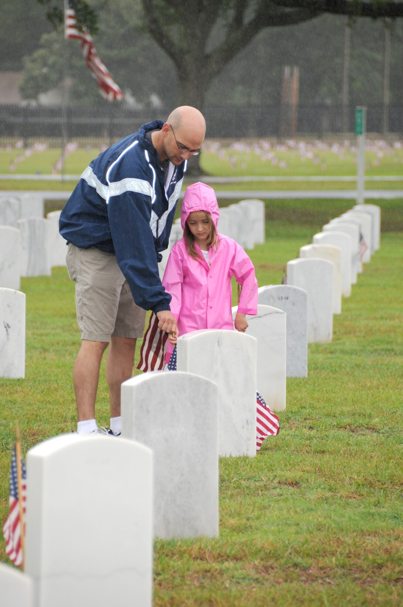 Tech. Sgt. Kerry Holmes and his 7-year-old daughter, Emily, were among the Keesler volunteers who braved the rain to place flags on the graves at Biloxi National Cemetery.  (U.S. Air Force photo by Kemberly Groue)