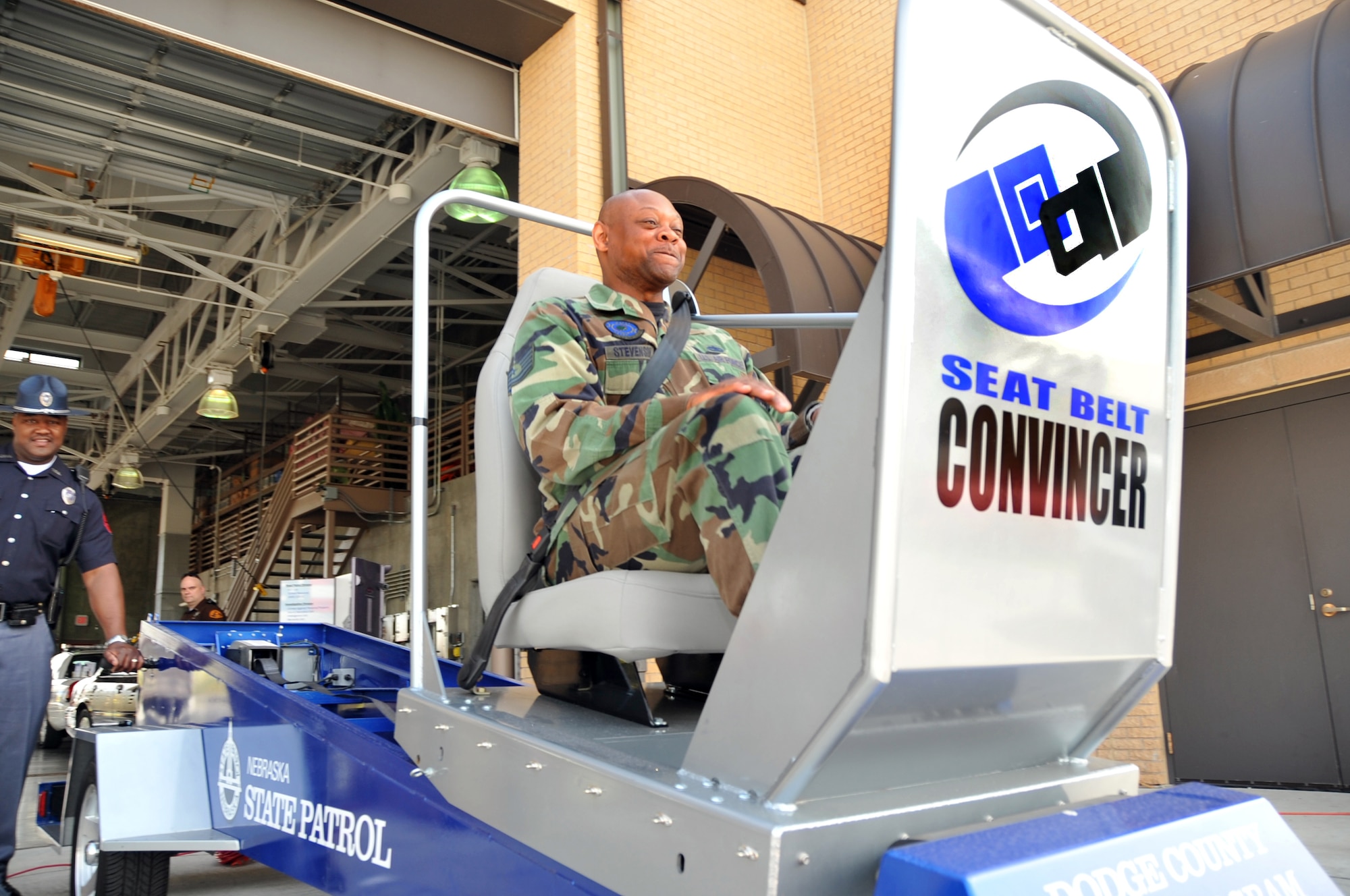 OFFUTT AIR FORCE BASE, Neb. -- Tech Sgt. Darrell Stevenson, munitions flight chief with the 55th Maintenance Squadron, experiences the Seat Belt Convincer, as Officer Keith Bell of the Nebraska State Police Community Policing Division,looks on during a safety fair at the Offutt Fire House May 21. Officer Bell said the five to seven mile-an-hour crash simulator allows people to feel the effects of a crash at a low speed. The safety fair was part of Offutt's annual Safety Day, which focuses on reminding all Airmen to practice safety on a daily basis. U.S. Air Force Photo by Jeff W. Gates
