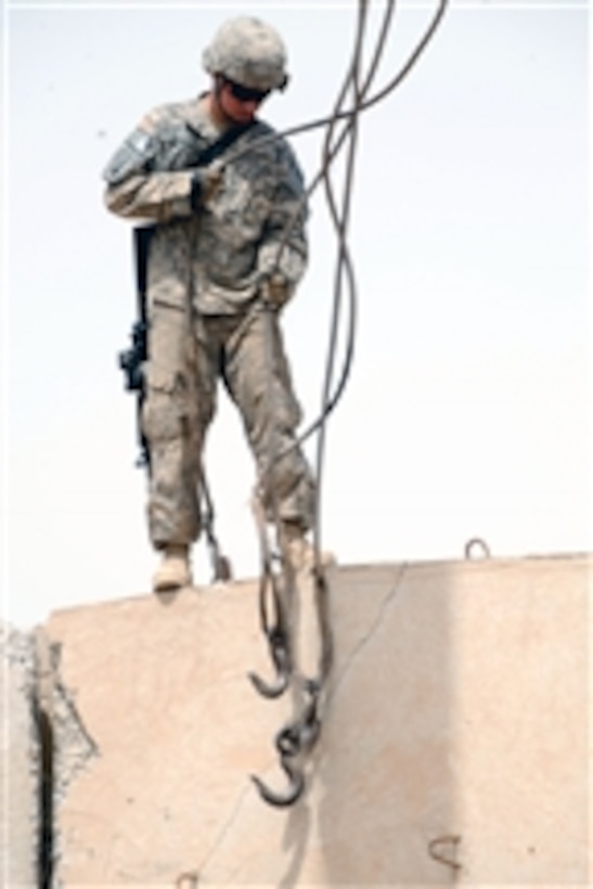 U.S. Army Spc. Calob Backes stands atop a concrete barrier preparing to hook up cables used to lift it into a new position at Joint Security Station Loyalty, in eastern Baghdad, Iraq, on May 17, 2009.  Backes is assigned to Headquarters and Headquarters Company, Brigade Special Troops Battalion, 3rd Brigade Combat Team, 82nd Airborne Division.  