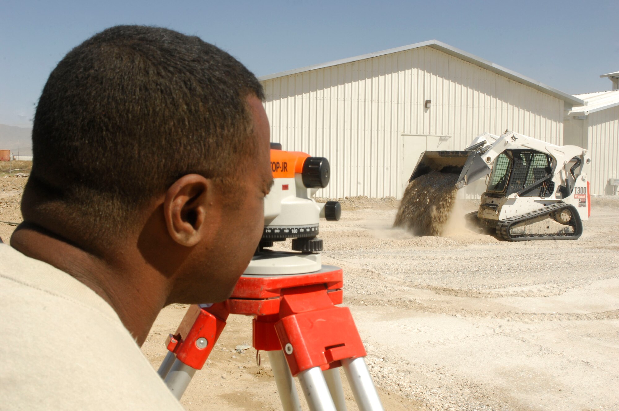 BAGRAM AIR FIELD, Afghanistan- Tech. Sgt. Darryl Guppy, 455th Expeditionary Civil Engineer Squadron, looks through an automatic level device while Airman 1st Class Sheldon Mellott, 455th ECES, pours dirt for an A-10 aircraft hangar extension project May 27. An auto level helps the technician determine how level the foundation is before concrete is poured. Thirteen civil engineer "Dirt Boys" have worked on the project that costs approximately $156,000. Sergeant Guppy hails from Brooklyn, N.Y., and is deployed from the Community College of the Air Force at Gunter Annex, Ala. Airman Mellott hails from Salt Lake City, Utah and is deployed from the 509th Civil Engineer Squadron at Whiteman Air Force Base, Mo. (U.S. Air Force photo/Senior Airman Erik Cardenas)