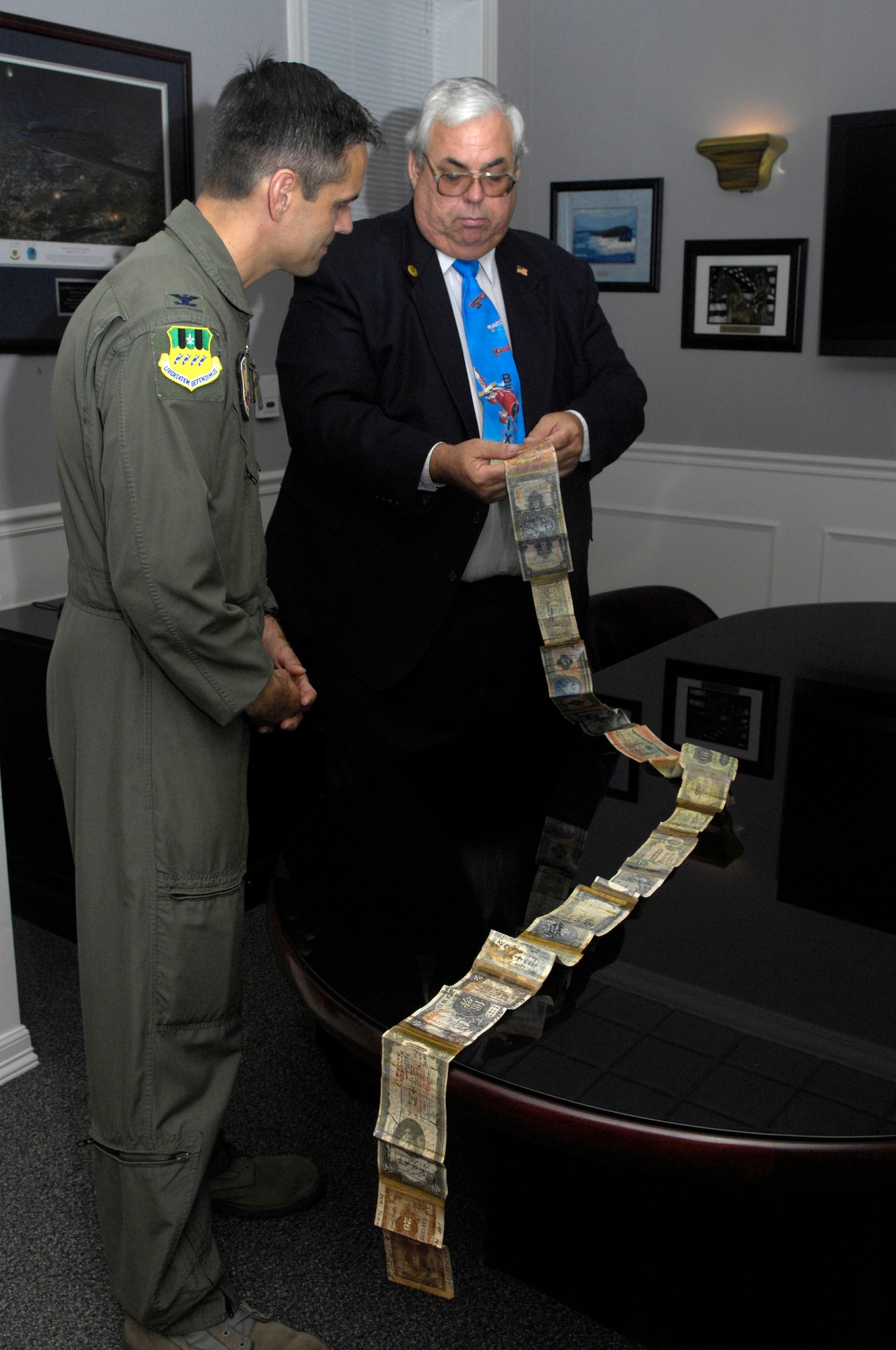 Joe Lawrence displays his father’s collection of foreign currency, which is called a short snorter, to Col. Steven Basham, 2d Bomb Wing commander May 21. The short snorter is known to have numerous signatures on it from witnesses of the servicemembers ventures. Colonel Basham added his name to the more than 100 already on it.