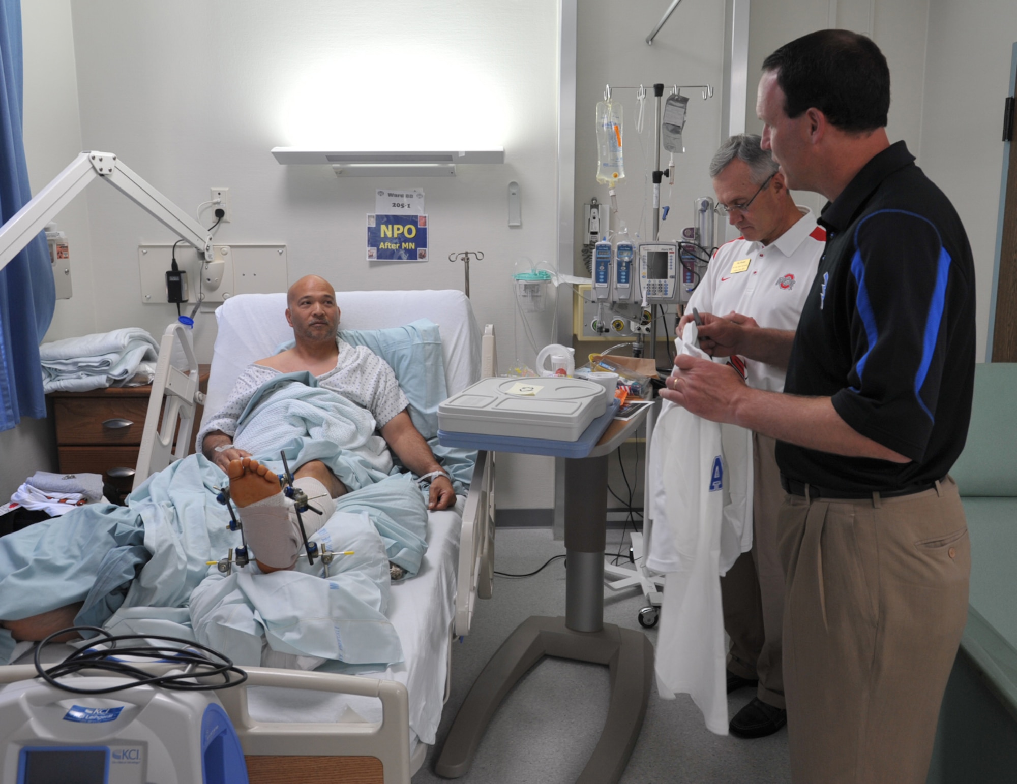 NCAA football coaches, Troy Calhoun of Air Force and Jim Tressel of Ohio State, visits with Henry Bautista at a U.S. military hospital in Landstuhl, Germany. The hospital was one of the first stops for Coaches Tour 2009, a morale-boosting mission that brings NCAA football coaches to U.S. servicemembers. Bautista served 10 years in Army intelligence without any major injuries before he became a civilian field representative for an armored vehicle contractor. He was flown to Germany from Iraq after his leg was severely injured by a mishap with one of the vehicles. The Coaches Tour is organized by Morale Entertainment, LLC., in association with Armed Forces Entertainment. (U.S. Air Force photo/Tech. Sgt. Jason Schaap)