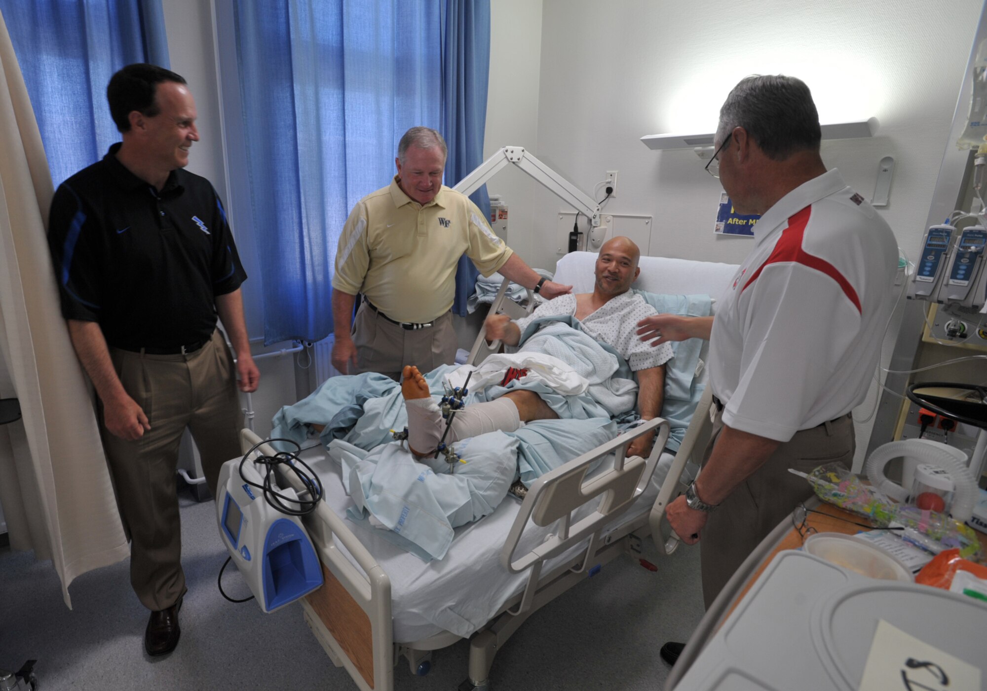 NCAA football coaches, Troy Calhoun of Air Force, Jim Grobe of Wake Forest, and Jim Tressel of Ohio State, visit with Henry Bautista at a U.S. military hospital in Landstuhl, Germany. The hospital was one of the first stops for Coaches Tour 2009, a morale-boosting mission that brings NCAA football coaches to U.S. servicemembers. Bautista served 10 years in Army intelligence without any major injuries before he became a civilian field representative for an armored vehicle contractor. He was flown to Germany from Iraq on May 26 after his leg was severely injured by a mishap with one of the vehicles. The Coaches Tour is organized by Morale Entertainment, LLC., in association with Armed Forces Entertainment. (U.S. Air Force photo/Tech. Sgt. Jason Schaap)