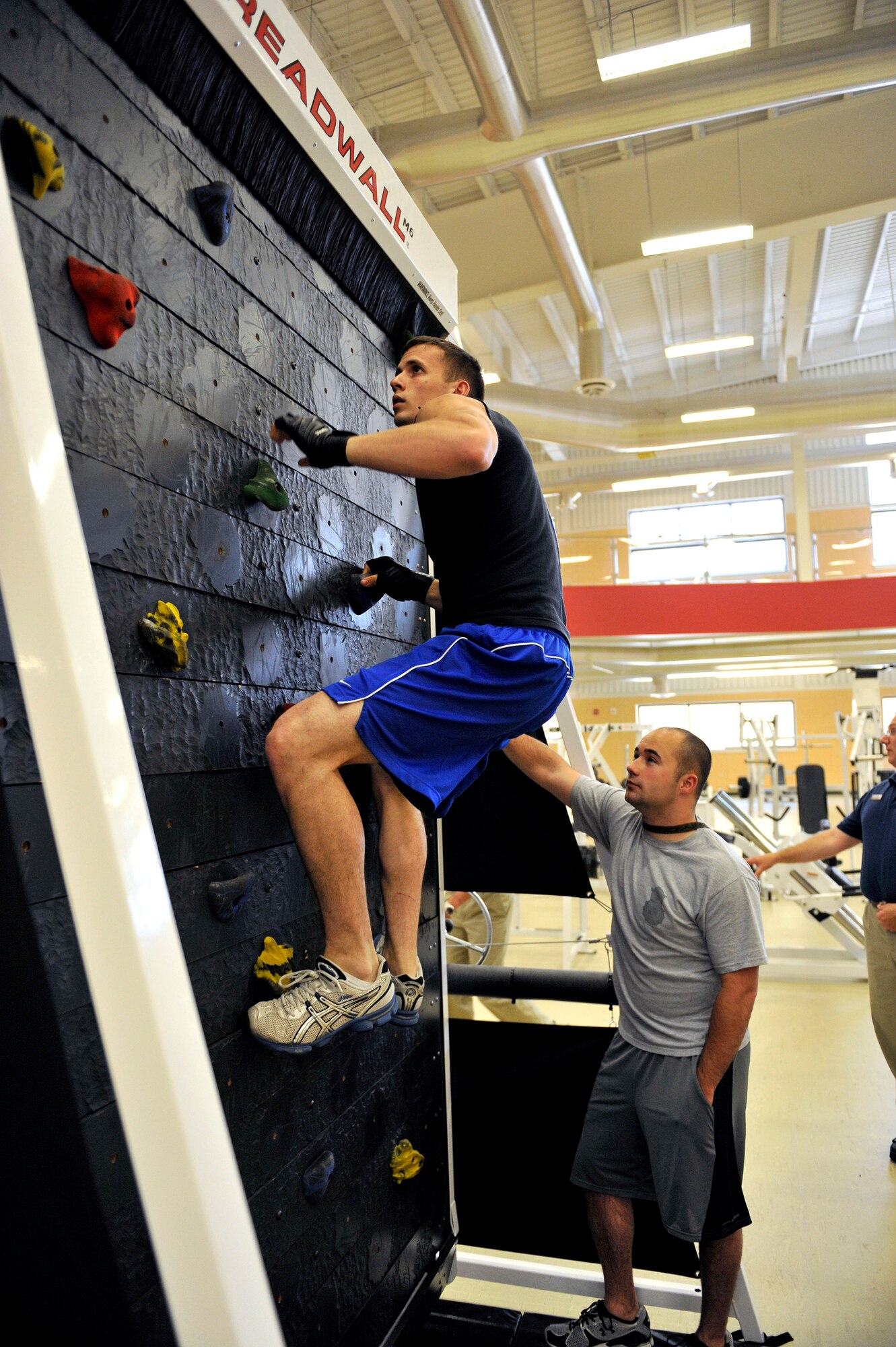Senior Airman Tim McCoy, 741st Missile Security Forces Squadron member, scales the treadwall in a climbing competition May 27 during the new Fitness Center's grand opening.  Airman McCoy took first in the event by climbing the most number of revolutions within three minutes.  Senior Airman Dave McComb, also of 741st MSFS, adjusts the speed of the moving rock wall. (U.S. Air Force photo/John Turner)