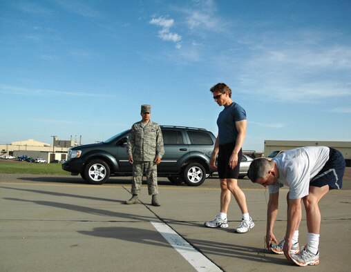 Staff Sgt. Kwinton Estacio, 341st Force Support Squadron fitness specialist, waits for Eric Thayer, 341st FSS community support consultant and Maj. Charles Ashmore, 341st FSS commander, to stretch before a timed mile-and-a-half run during an Air Force fitness test May 19 on the flight line. Mr. Thayer scored 100 points, clinching five perfect scores in a row in as many years. (U.S. Air Force photo/Senior Airman Dillon White)