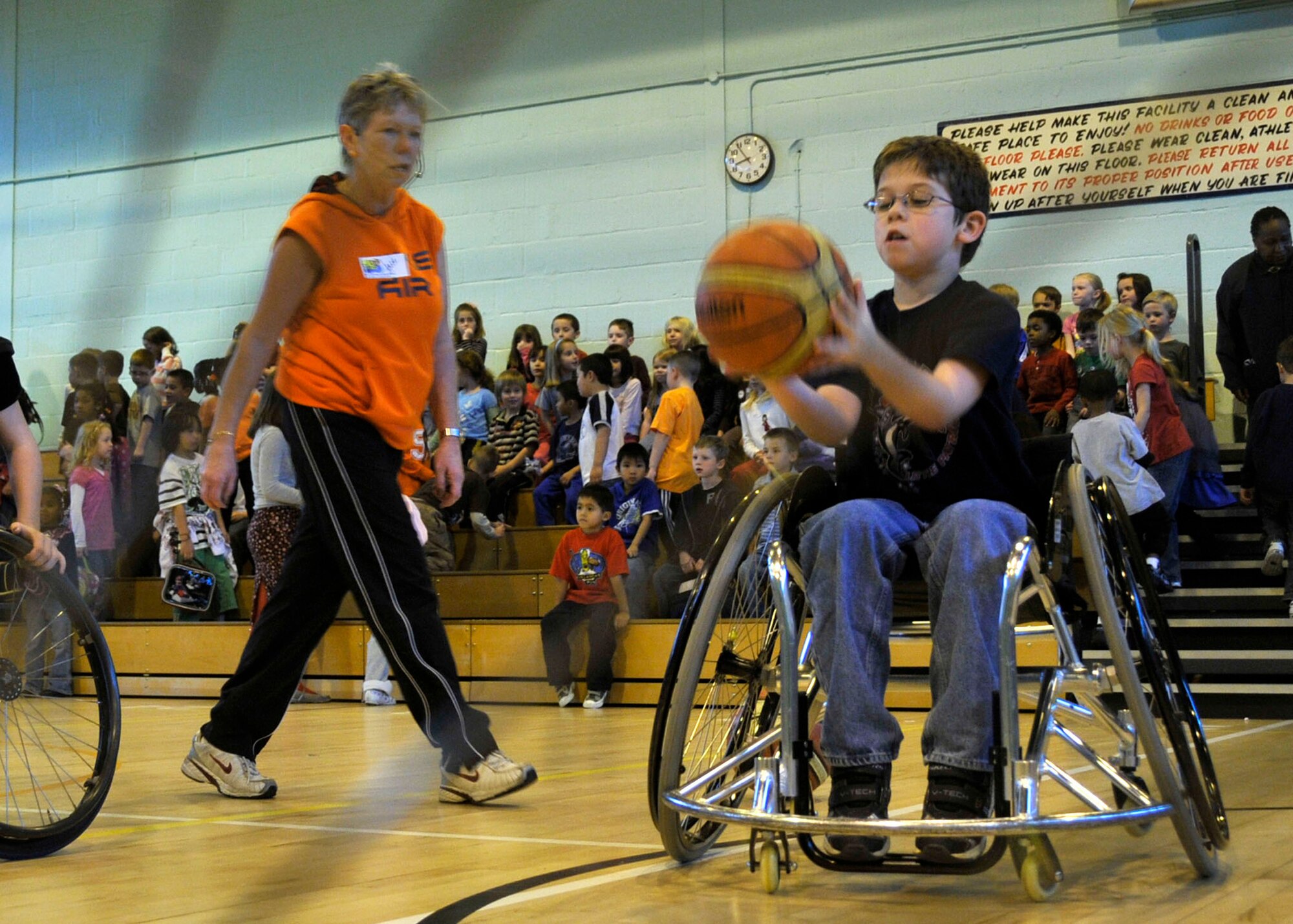 Alexander, 3rd grader, passes the ball to his teammate as Jill Anderson, Bury Bombers wheelchair basketball coach, observes at RAF Lakenheath Oct. 27. Alexander was part of a wheelchair basketball demonstration team for Lakenheath Elementary, giving the students hands on experience of the sport. (U.S. Air Force photo by Airman 1st Class Eboni Knox) 