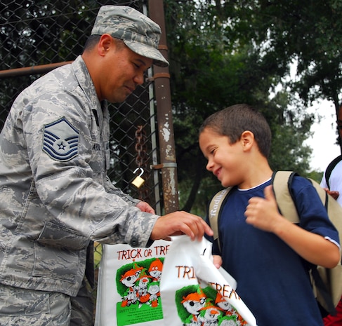 Master Sgt. Erwin Arguilla gives Alex Serrano a colorful trick-or-treat bag at the Lamb's Elementary School gate here Oct. 30. Members of the 437th Airlift Wing Safety Office provided students passing through both the Lamb's and Hunley Park Elementary School gates free bags for collecting Halloween candy and reminded each to have a safe Halloween. Sergeant Arguilla is the 437 AW Safety Office ground safety superintendent and Alex is the son of Staff Sgt. Kevin Serrano who is with the 437th Logistics Readiness Squadron. (U.S. Air Force photo/Staff Sgt. Daniel Bowles)