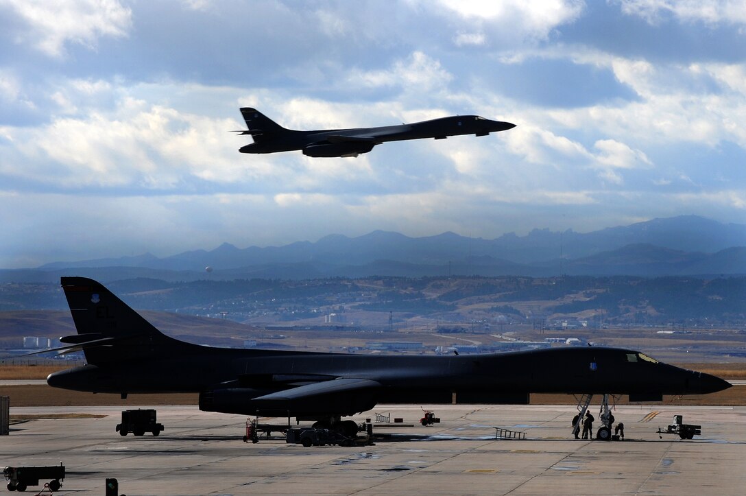 ELLSWORTH AIR FORCE BASE, S.D. -- A B-1B Lancer receives maintenance as another B-1 flies over head, Nov. 2. The B-1B can rapidly deliver massive quantities of precision and nonprecision weapons against any adversary, anywhere in the world. (U.S. Air Force photo/Airman 1st Class Joshua J. Seybert)